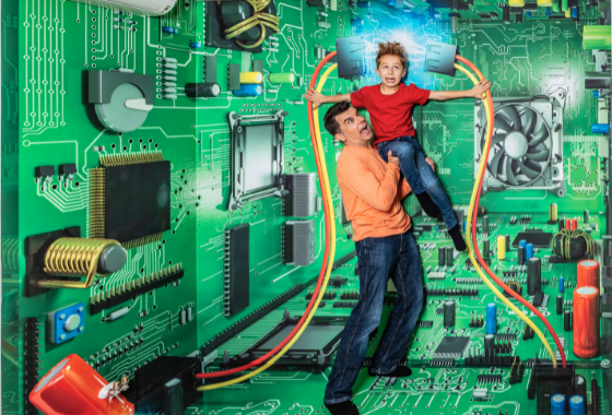 Een man en een kind staan voor een grote 3D-illusie van een groene printplaat met elektronische componenten en draden.