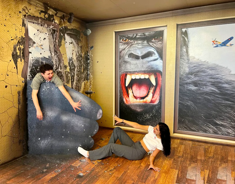 Twee mensen poseren met 3D-illusiekunst met een gigantische gorilla-kop en een grote hand in een museumzaal