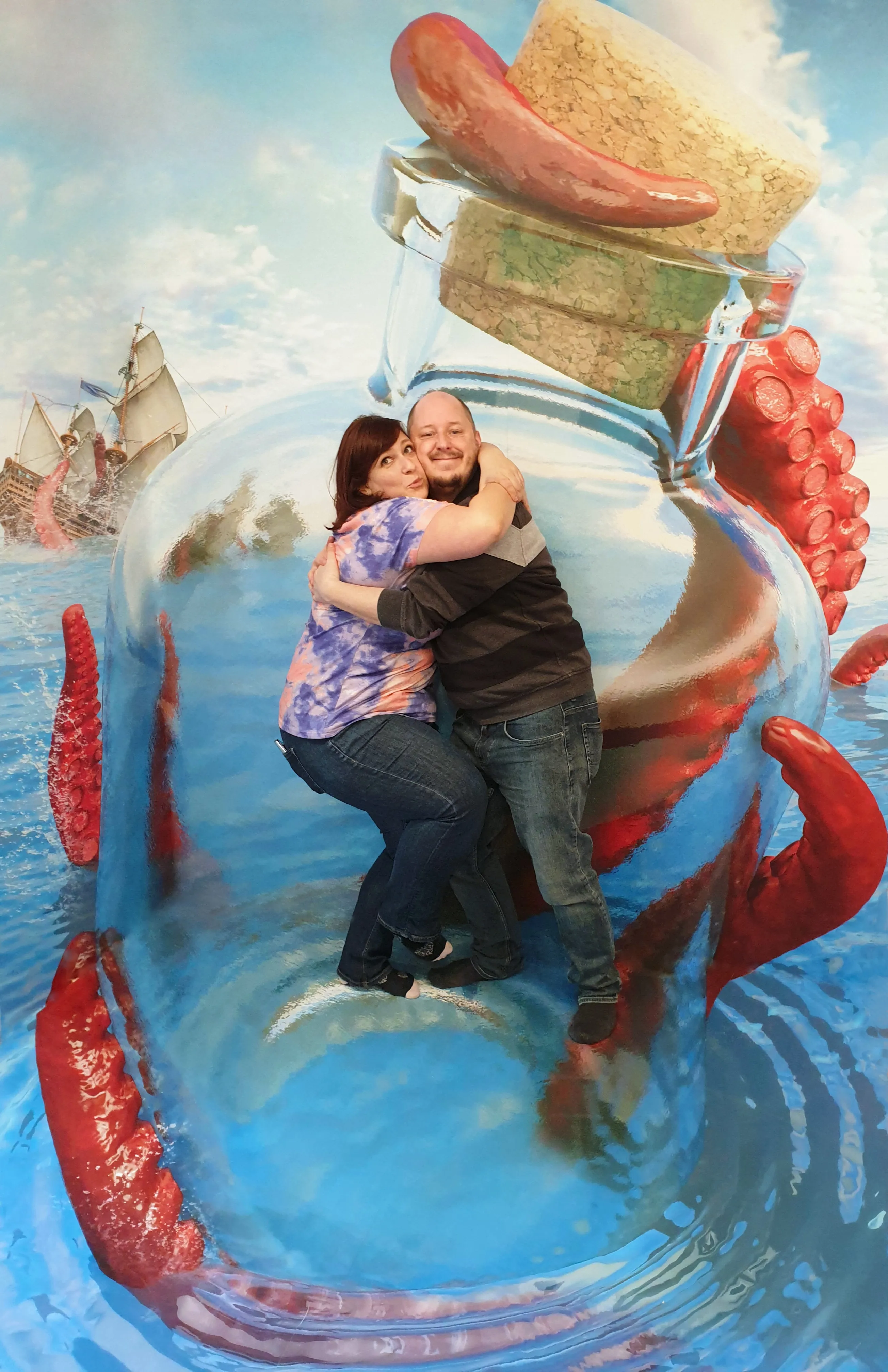 Een man en vrouw die elkaar omhelzen in een grote 3D-illusie van een glazen fles met een octopus en een schip op de achtergrond