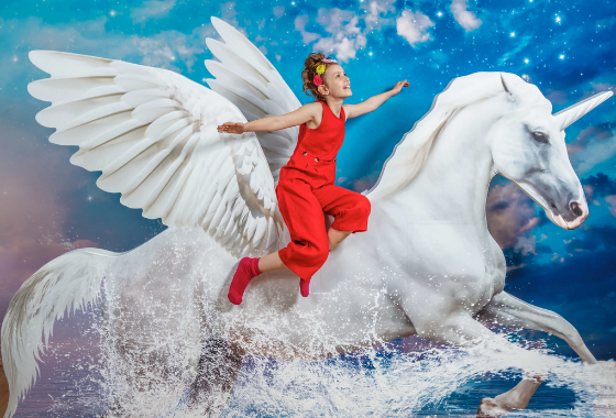 Een persoon in een rood jumpsuit die op een witte eenhoorn met vleugels rijdt tegen een blauwe sterrenhemel