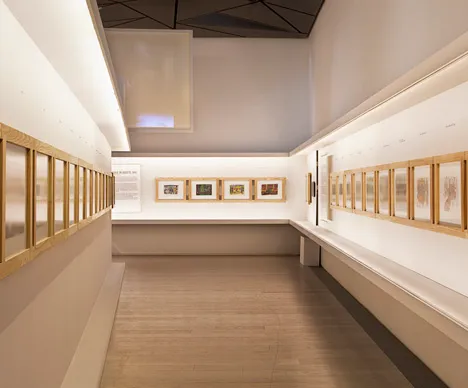 długa galeria-korytarz z oprawionymi dziełami sztuki na białych ścianach i drewnianych podłogach