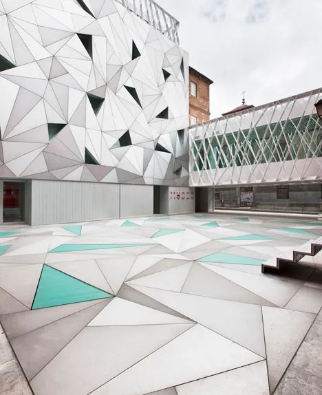 A modern building with a white geometric facade and a patterned courtyard with teal accents
