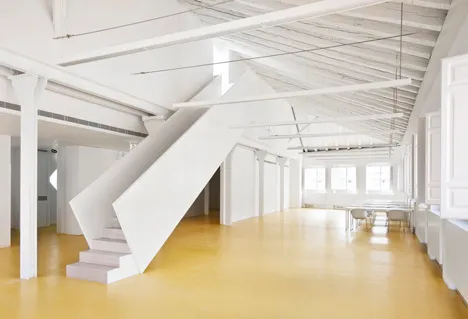 Interior of a museum with a white staircase, yellow floor, and exposed ceiling beams