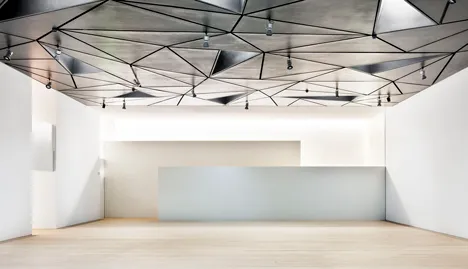 Modern gallery interior with white walls and a geometric metallic ceiling