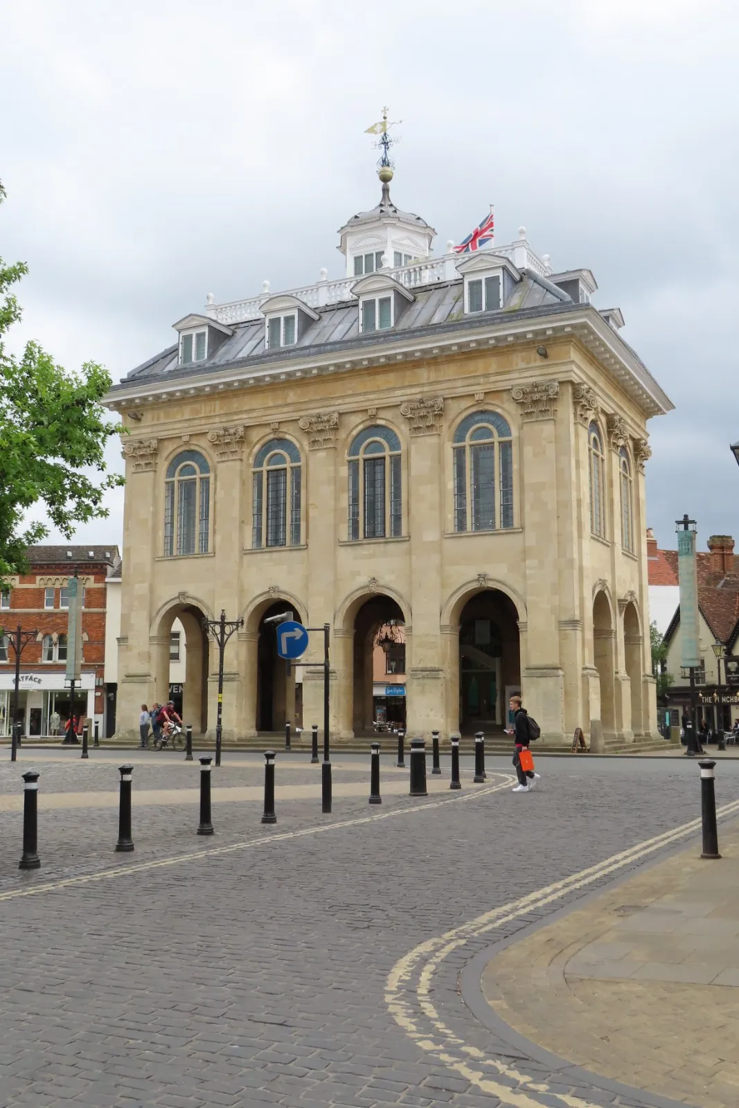 El Abingdon County Hall Museum, un histórico edificio de piedra con entradas arqueadas en la planta baja y grandes ventanales en la planta superior, situado en una plaza pavimentada.