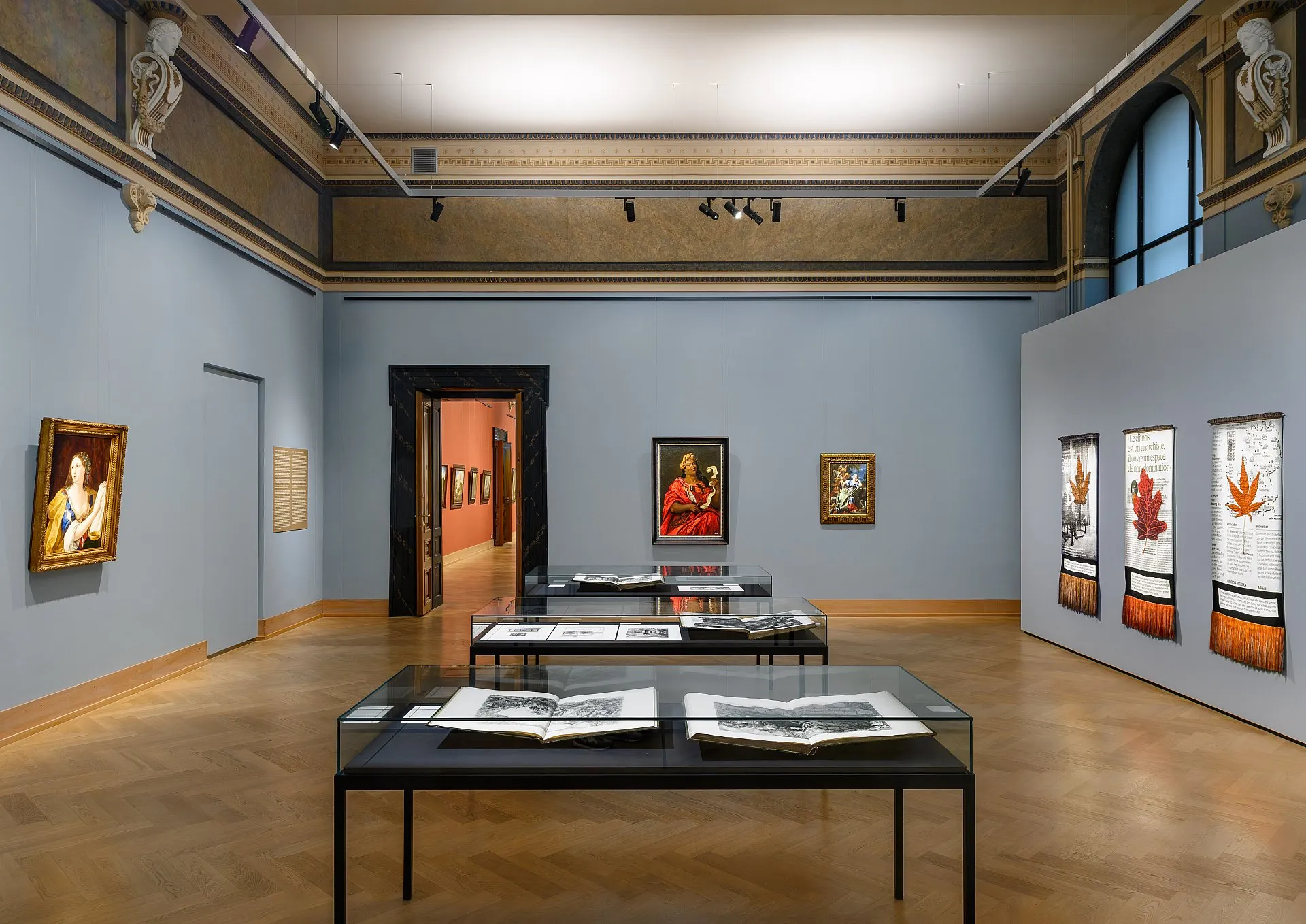 Gallery room with paintings on light blue walls and open books on tables