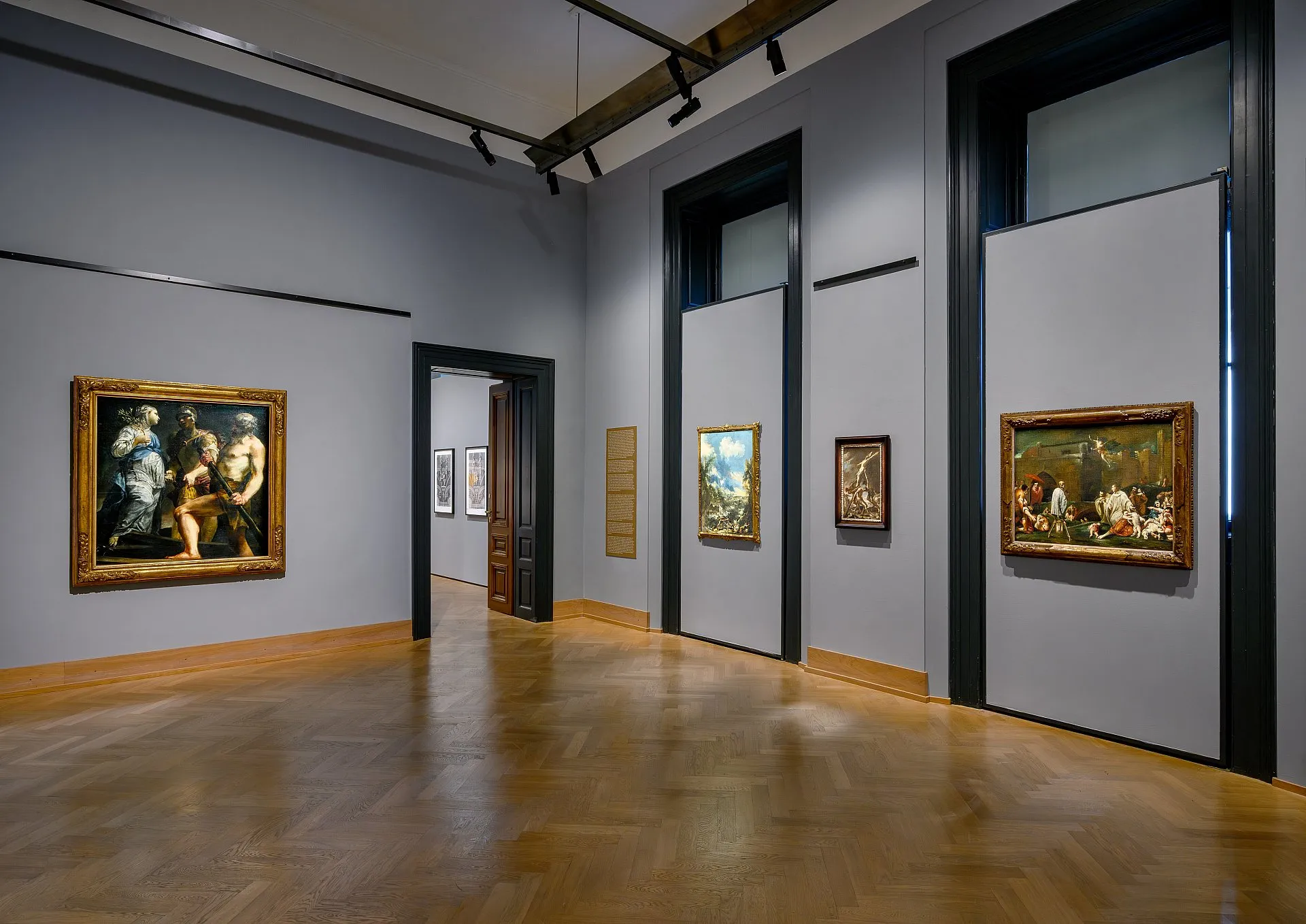 Galeria z obrazami na jasnoszarych ścianach i drewnianych podłogach