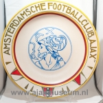 Biały ceramiczny talerz z napisem 'AMSTERDAMSCHE FOOTBALL CLUB AJAX' wokół krawędzi i niebieskim logo pośrodku, czerwone i żółte akcenty