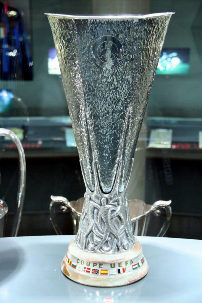 Trofeum Puchu UEFA z misternymi srebrnymi detalami i podstawą z flagami krajów, wystawione w gablocie muzealnej
