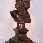 Bronze bust of a figure with a crown on a dark pedestal against a light background