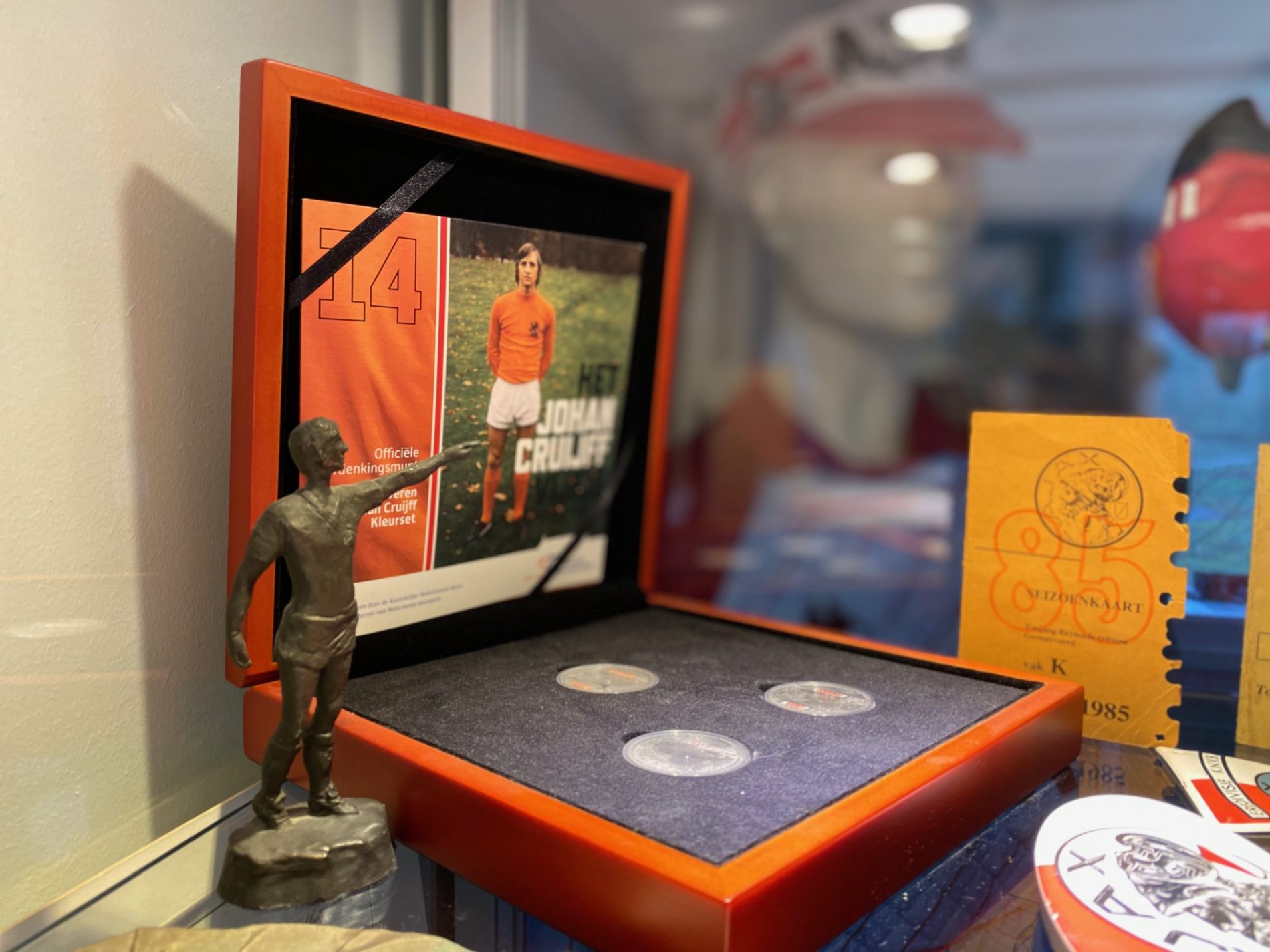 A display case with a small bronze statue, three silver coins, and a framed photo of a football player in an orange jersey with number 14.