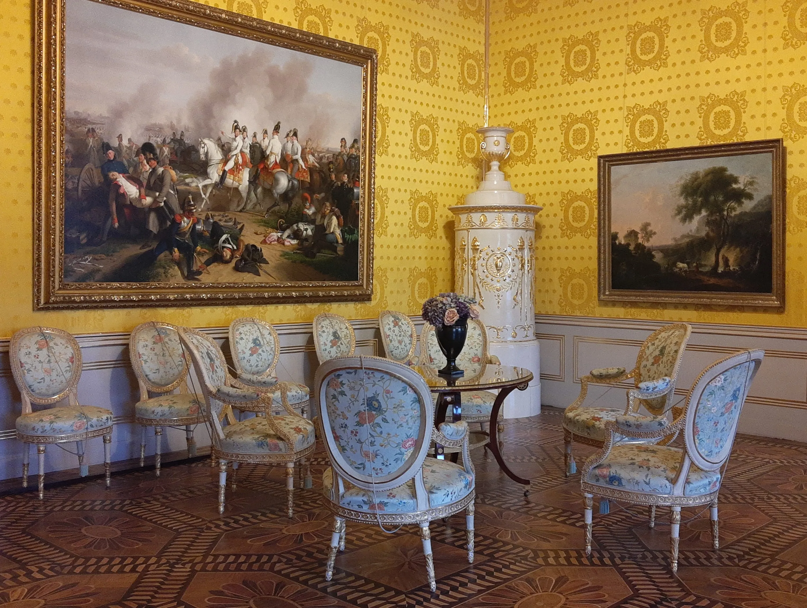 Ornate kamer met geel, geprint behang, een groot schilderij en een set lichtblauwe gestoffeerde stoelen rond een tafel