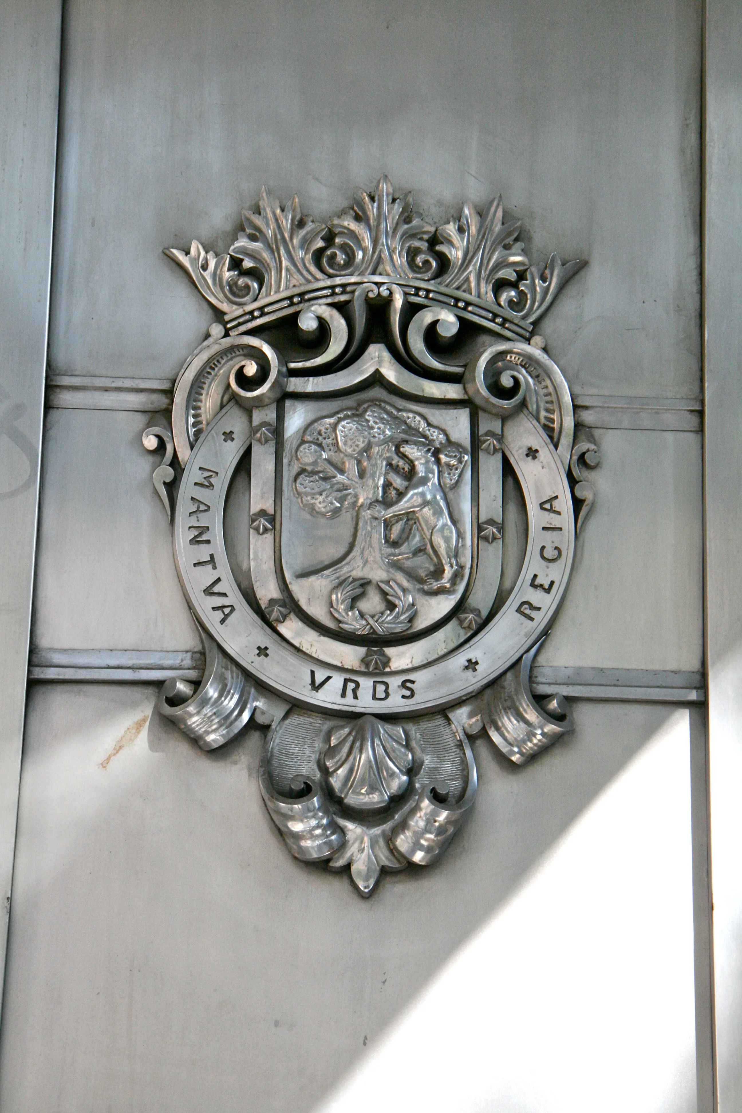 Ornato de escudo de armas de metal con un escudo coronado, árbol y figura, montado en la fachada de un edificio