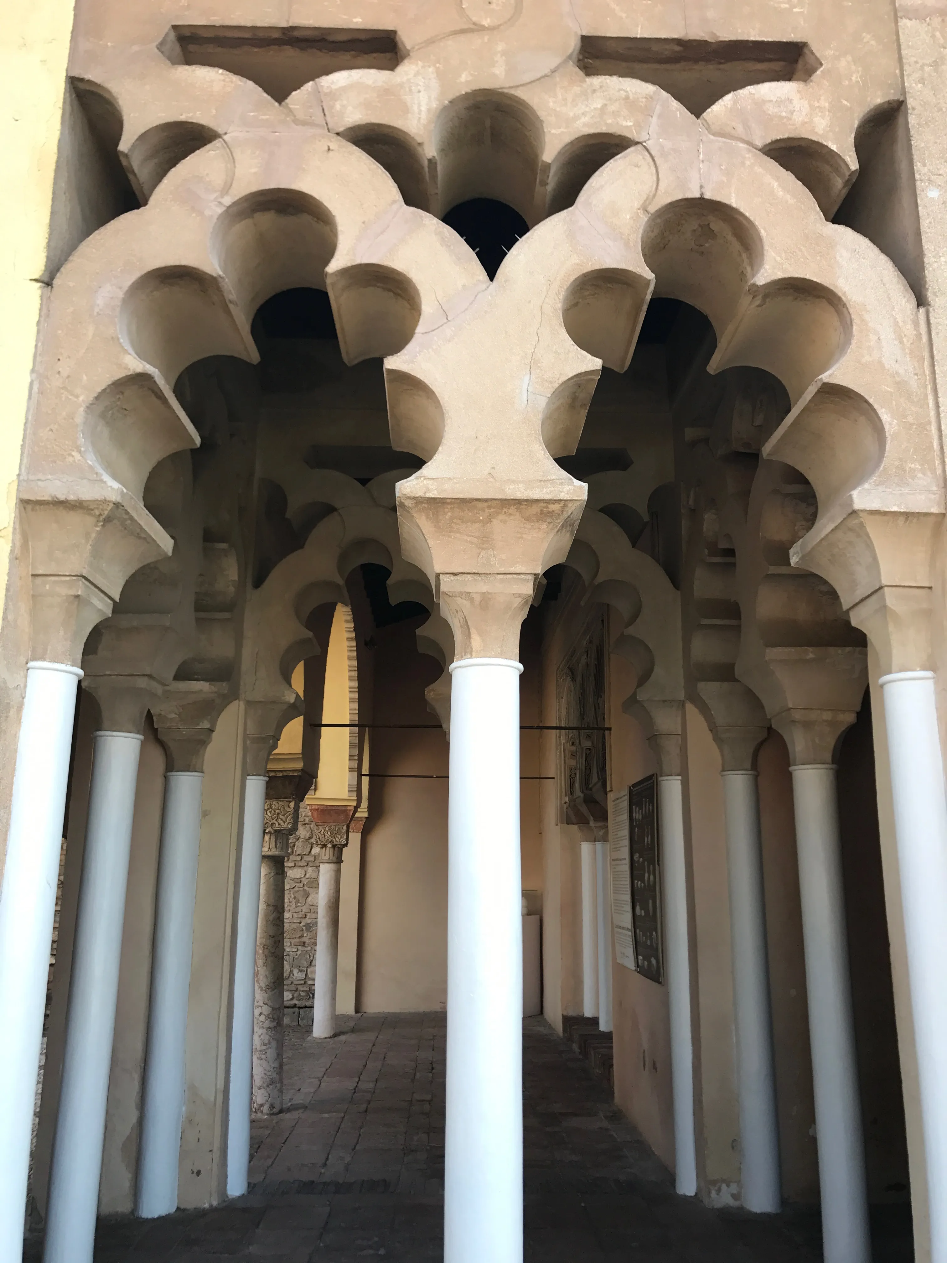 In elkaar grijpende polylobige Moorse bogen ondersteund door witte zuilen in een binnenplaats van het Alcazaba van Málaga.