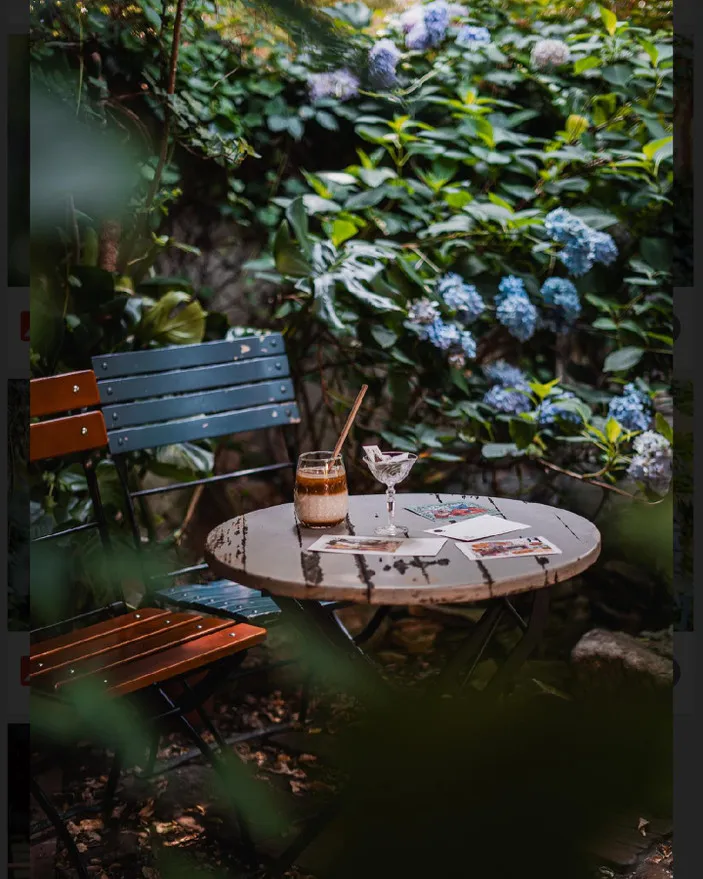 a round table with a coffee drink and a glass, surrounded by greenery and blue flowers