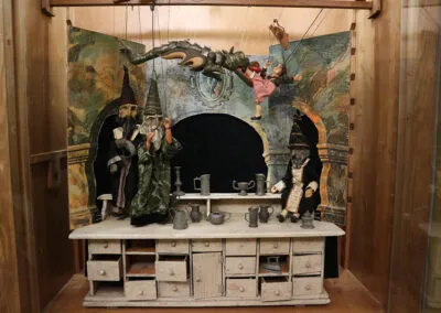 A display case with a theatrical scene including figures, a cauldron, and coffee equipment