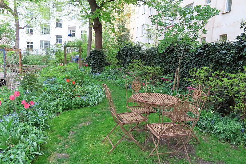 A garden with a metal table and chairs surrounded by green plants and flowers