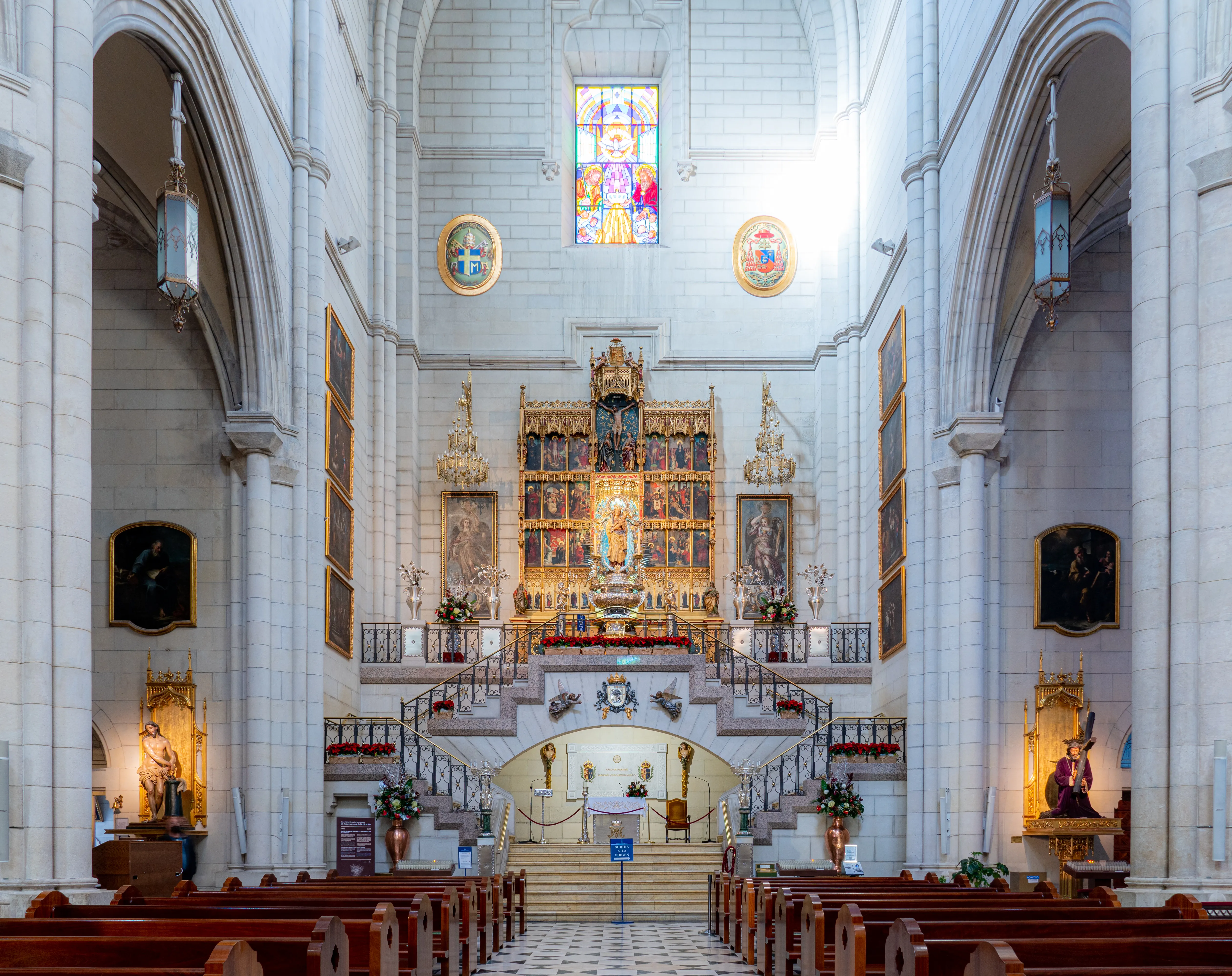 Interior of the Almudena Cathedral with a large altar, stained glass window, and rows of pews