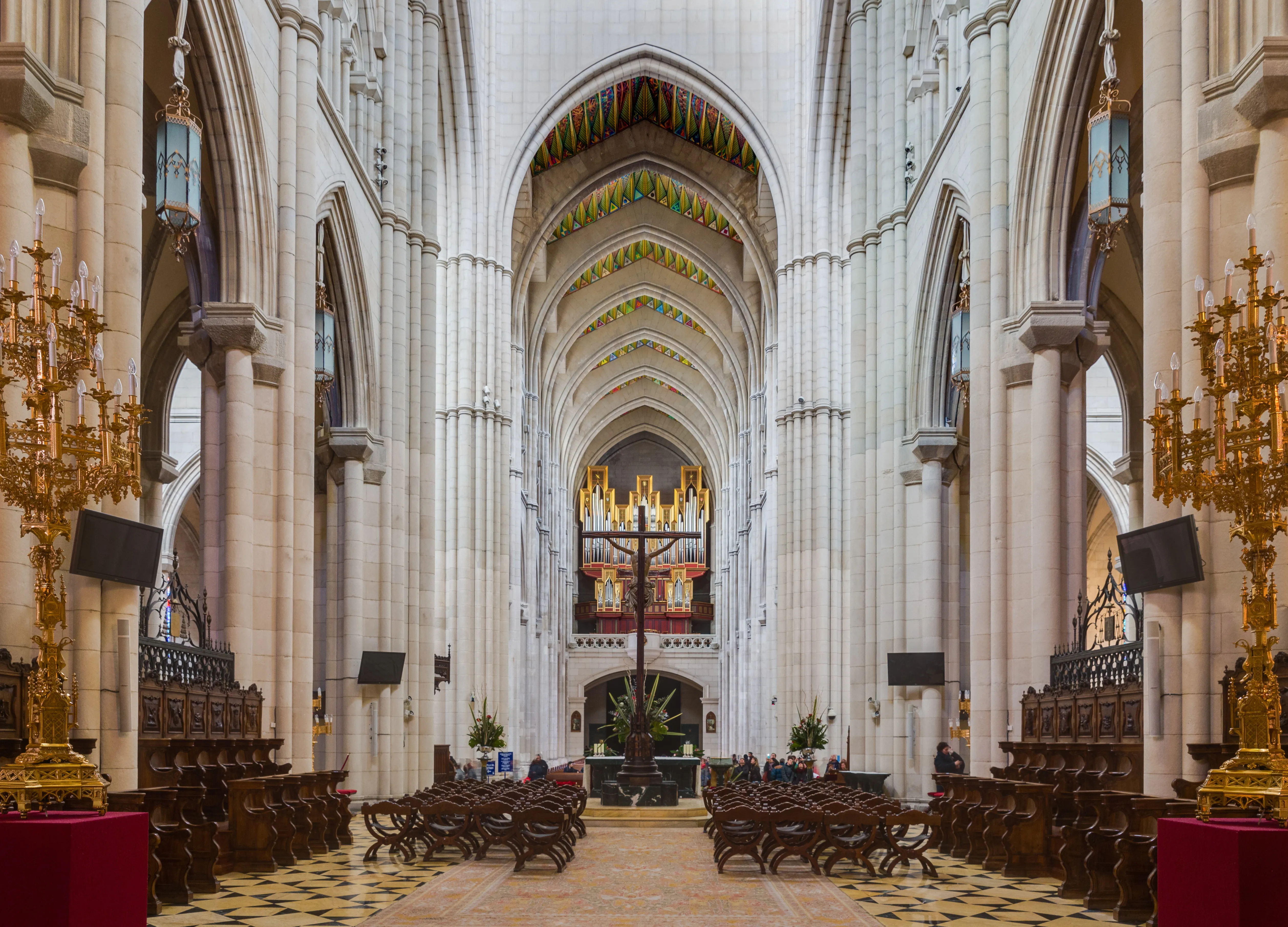 Interior of the Almudena Cathedral with tall stone columns, arched ceilings, and golden chandeliers
