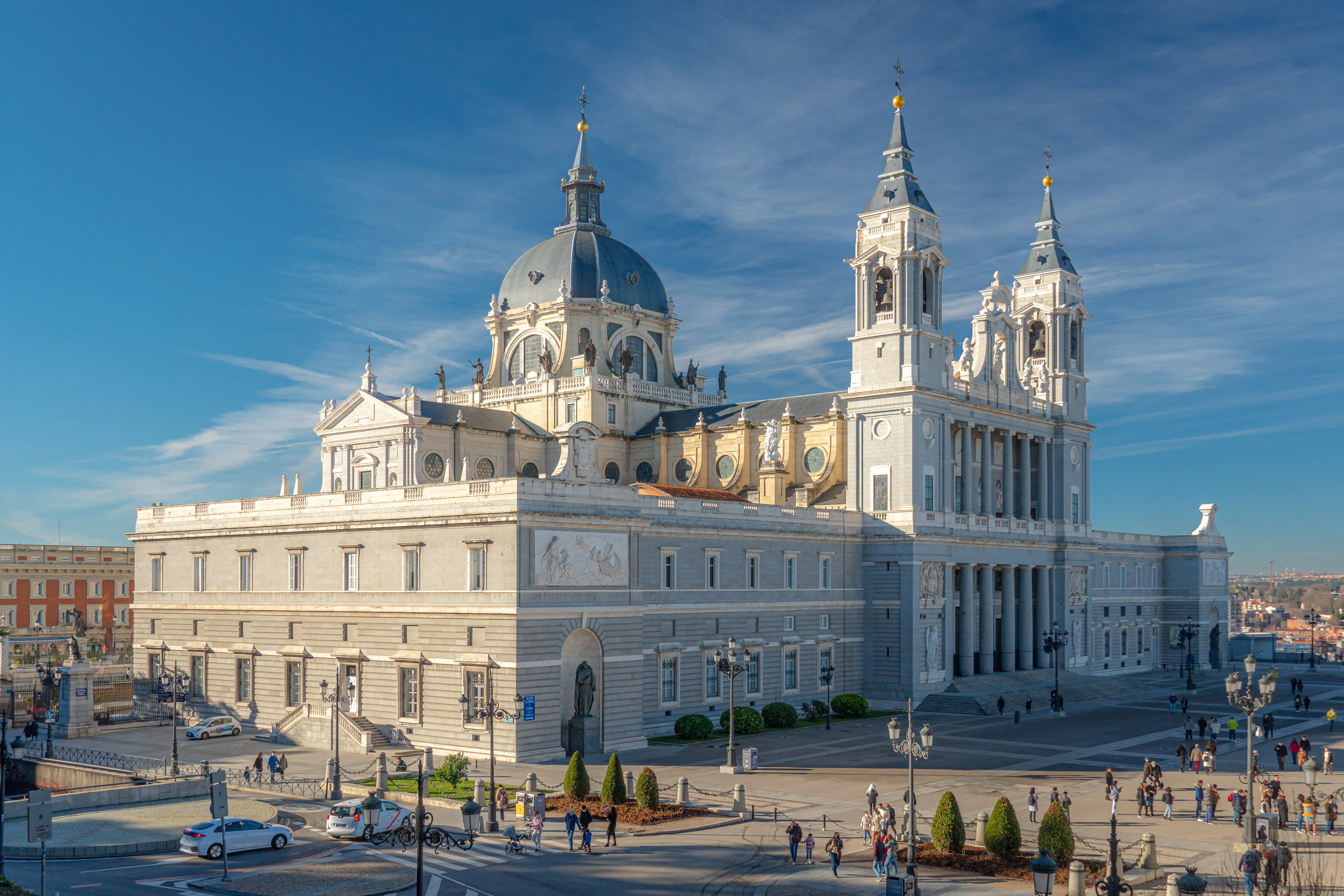 The Almudena Cathedral with its white facade, large dome, and twin towers under a blue sky with light clouds