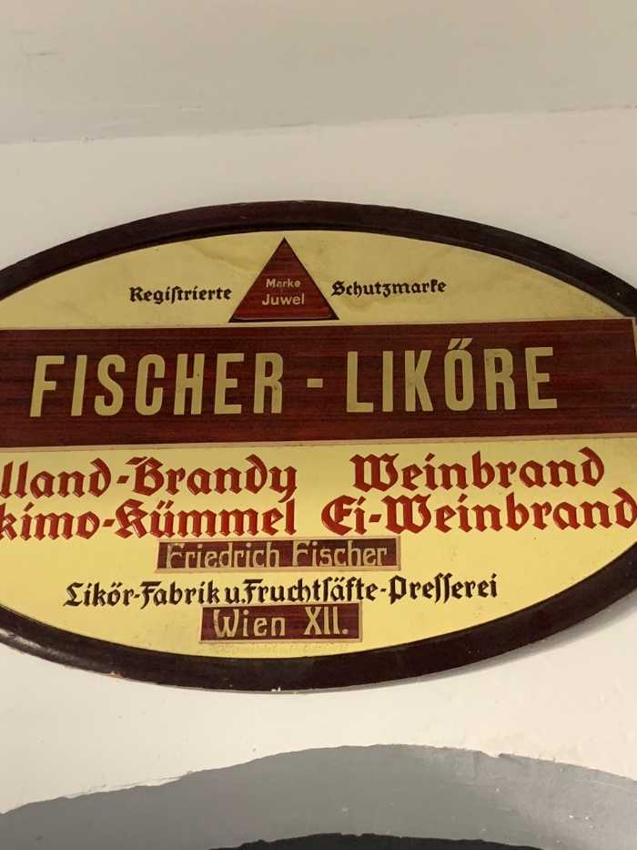 oval wooden sign with gold and red text reading Fischer-Liköre, Friedrich Fischer, and Wiener Schnapsmuseum