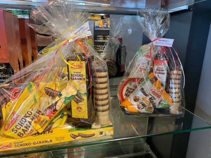glass shelf with two gift baskets wrapped in clear plastic, containing chocolate-covered banana snacks and other packaged treats