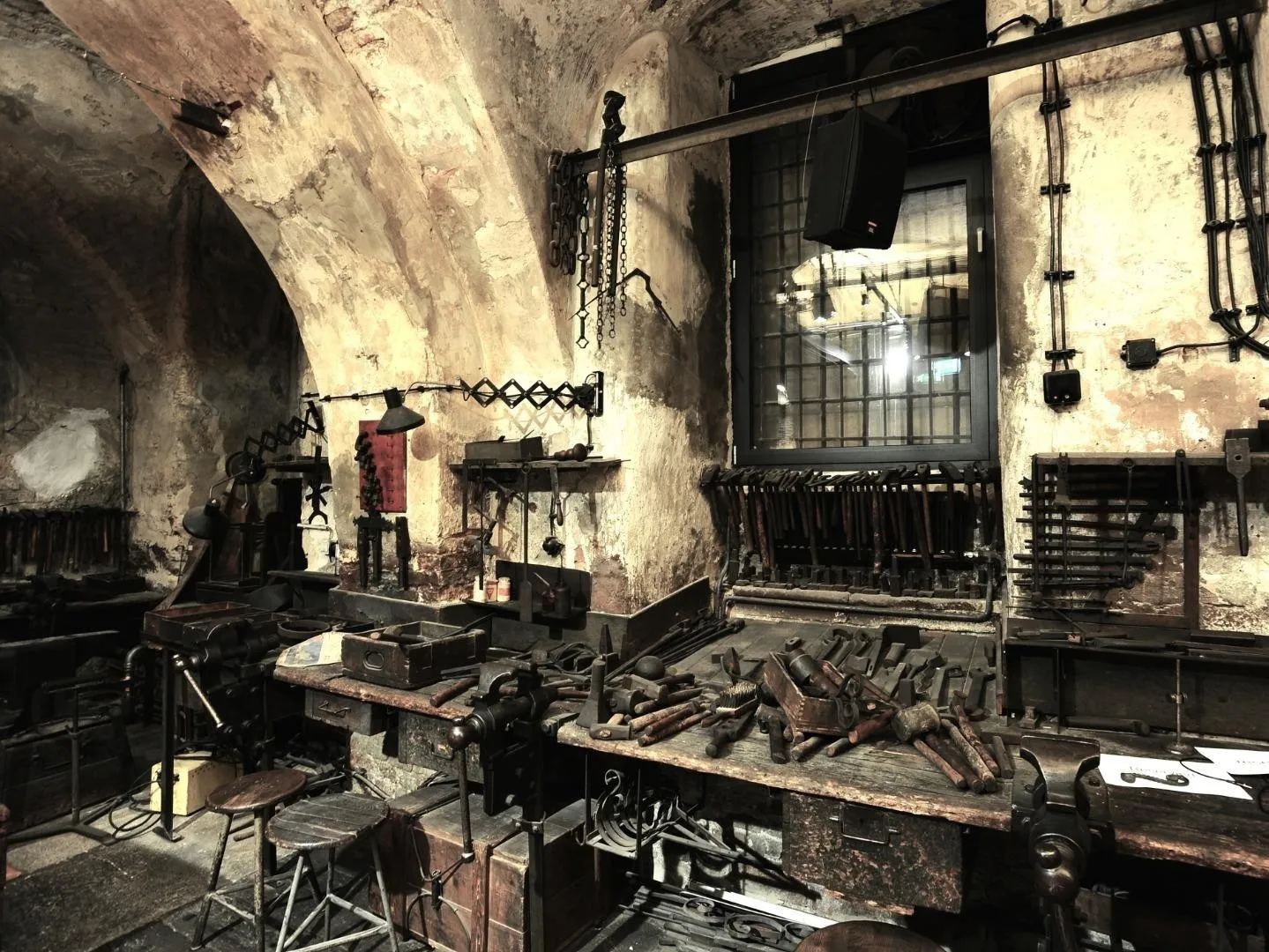 interior de un taller histórico con techos abovedados de piedra, bancos de trabajo y diversas herramientas de herrero
