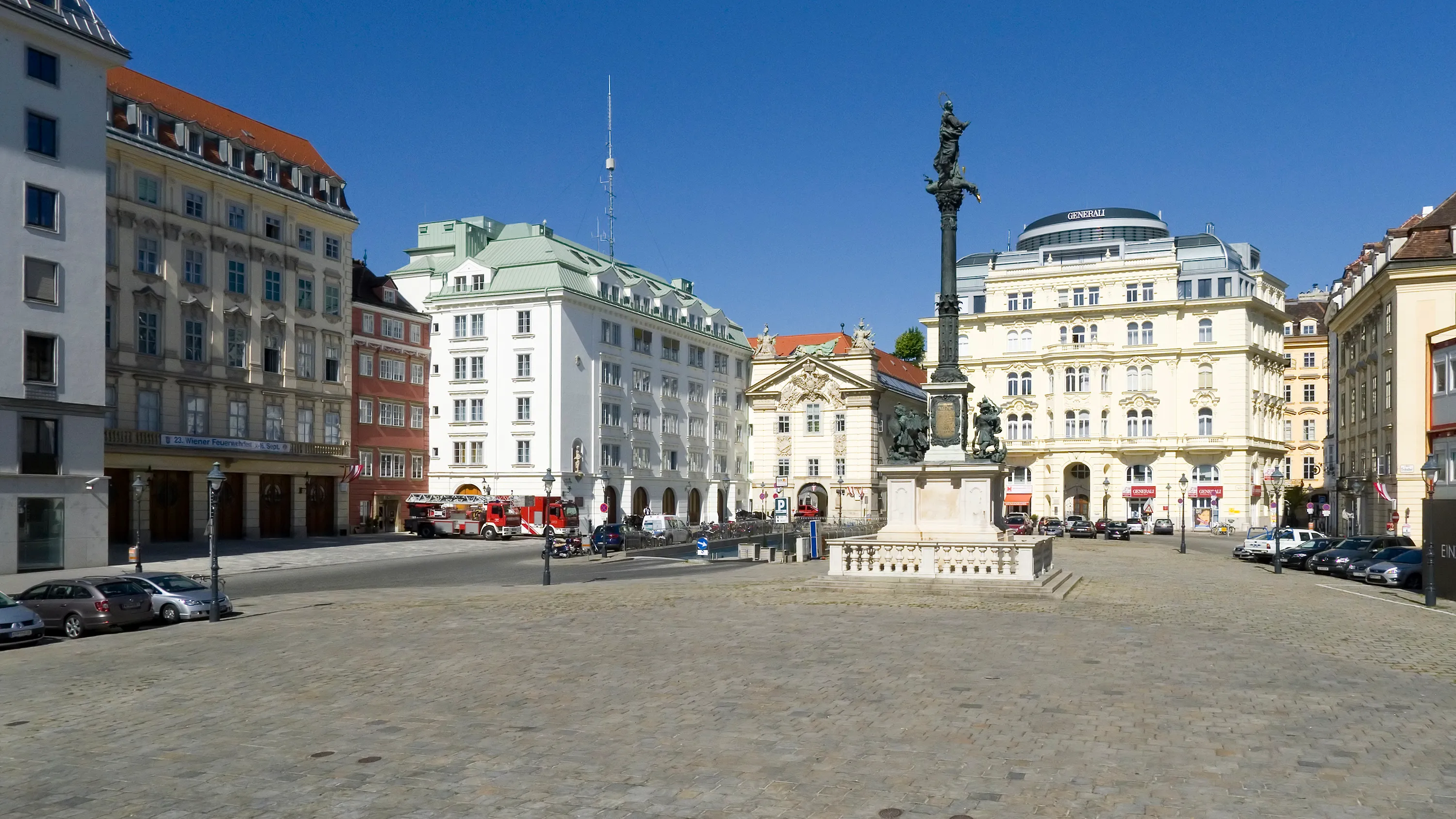 Rynek Am Hof z centralnym pomnikiem, otoczony zabytkowymi budynkami pod czystym, błękitnym niebem