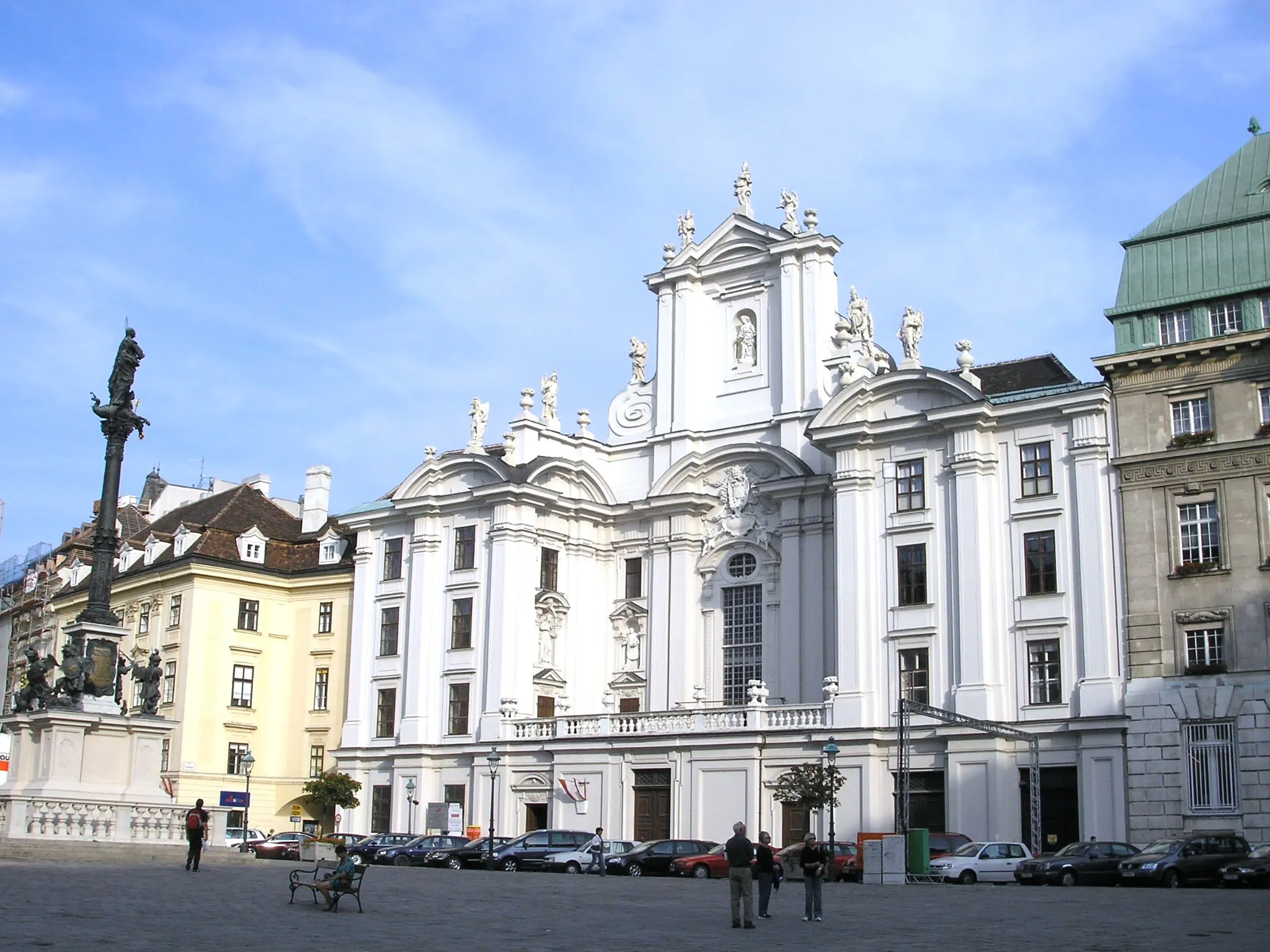Plac Am Hof z kościołem Minoritenkirche, wysoką kolumną ze statuą i zabytkowymi budynkami pod błękitnym niebem.