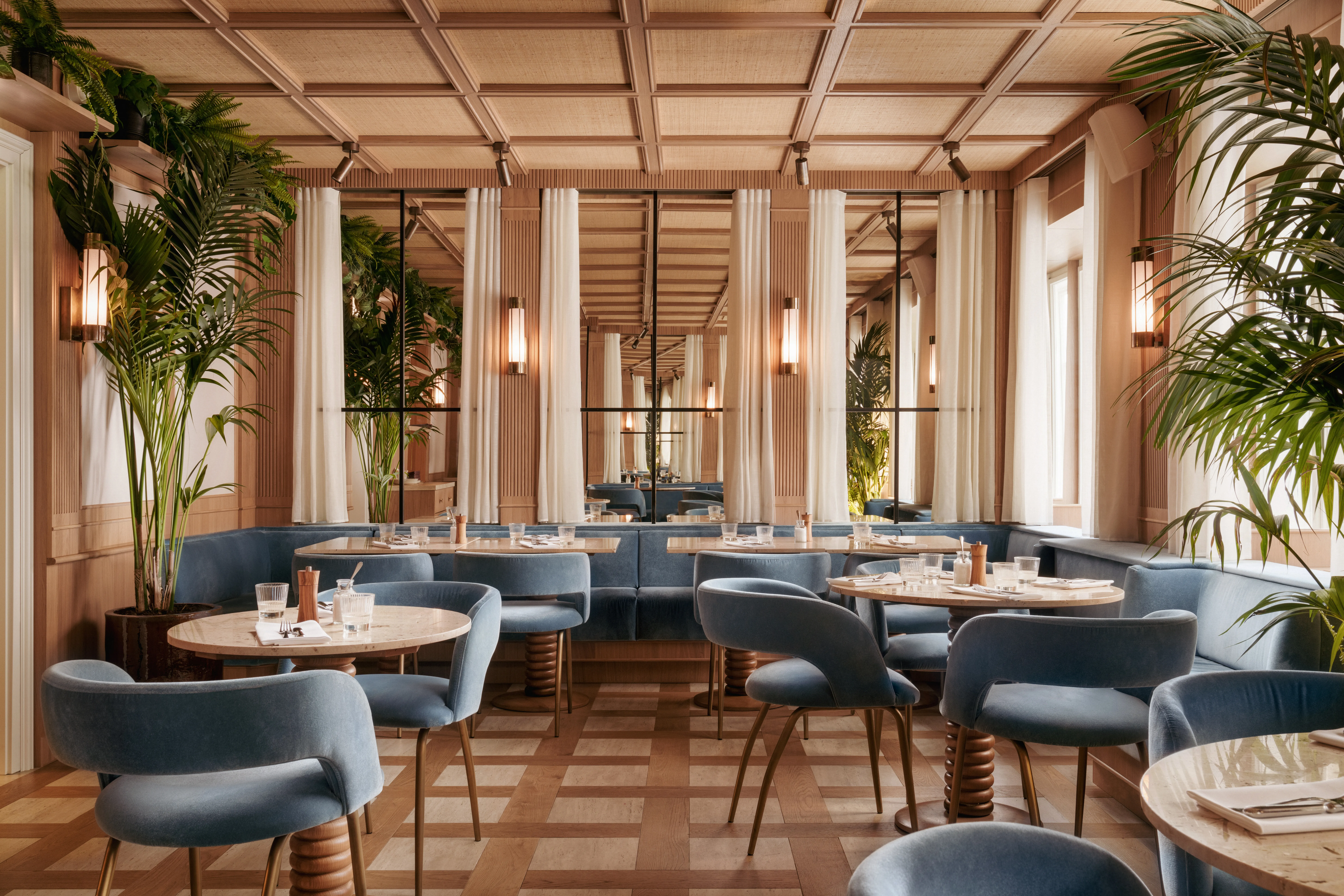 Wnętrze restauracji z niebieskimi krzesłami, okrągłymi stołami i kratkowaną podłogą