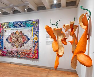 Kolorowy patchwork i pomarańczowe instalacje rzeźbiarskie wyeksponowane na białych ścianach w galerii muzealnej z drewnianą podłogą