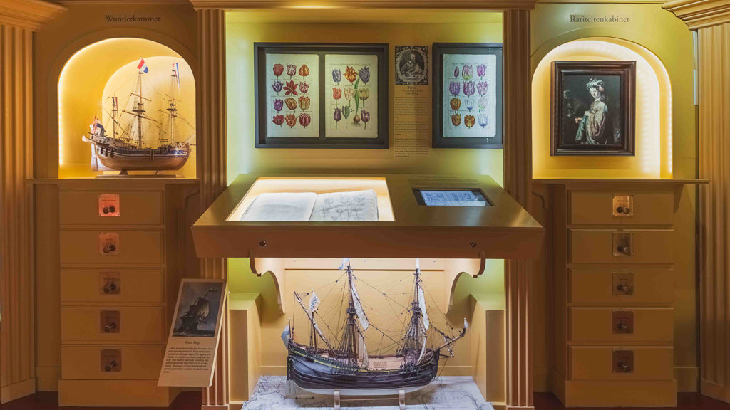 Museum interior with display cases containing model ships, framed heraldic emblems on yellow walls, and illuminated exhibits