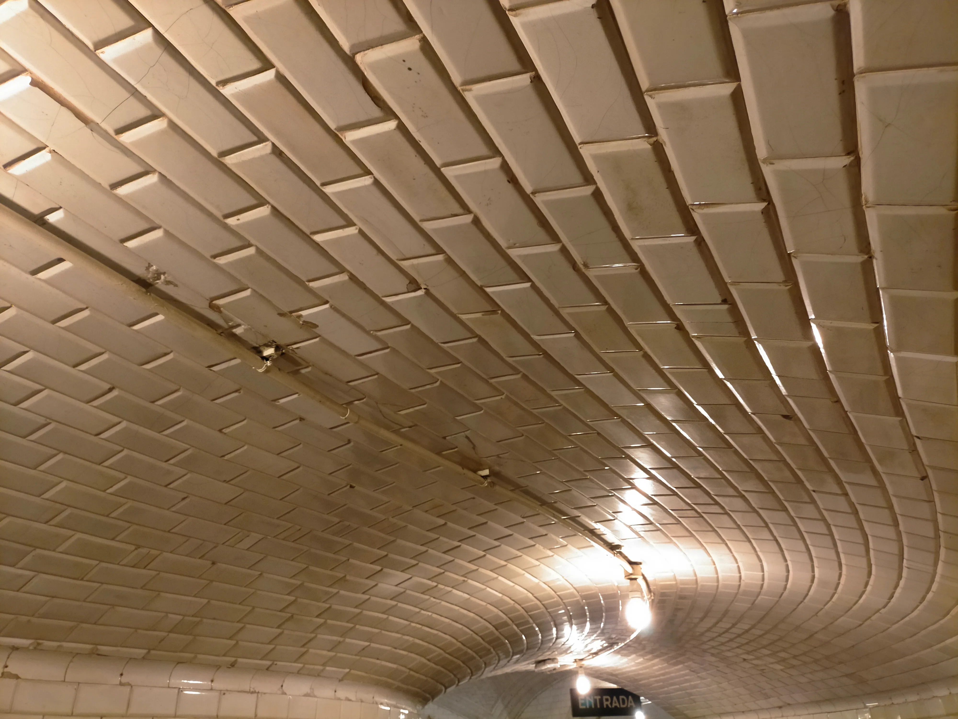 gebogen plafond met crèmekleurige tegels en vintage verlichtingsarmaturen in een metrostation