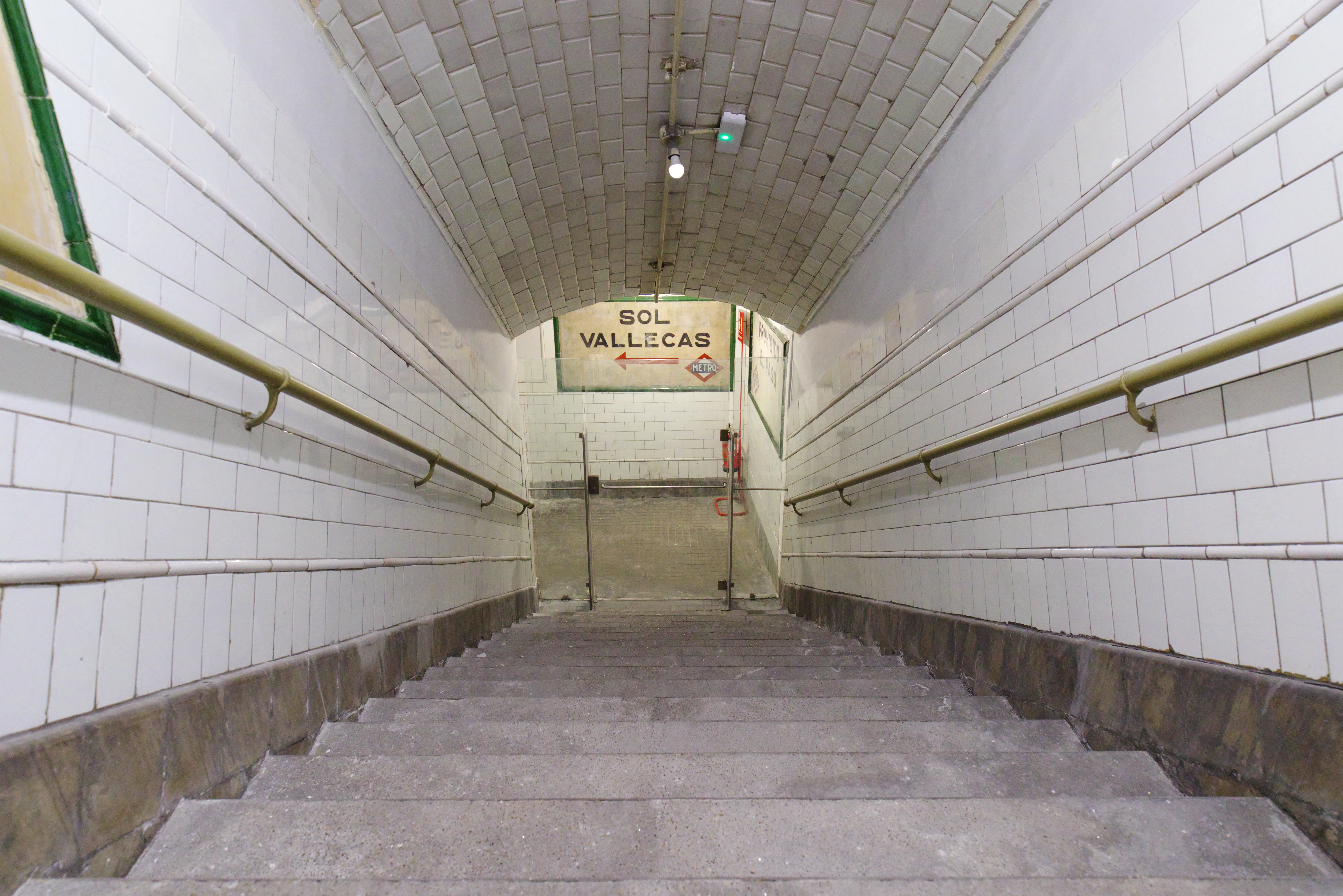 Trap die naar een metroperron leidt met witte betegelde muren en een bord met 'SOL VALLECAS'