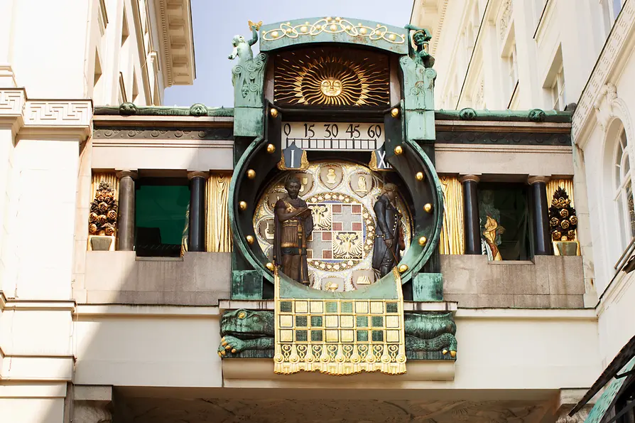 Art Nouveau klok met sculpturen van historische figuren en een zonneschijfontwerp op een gebouwgevel