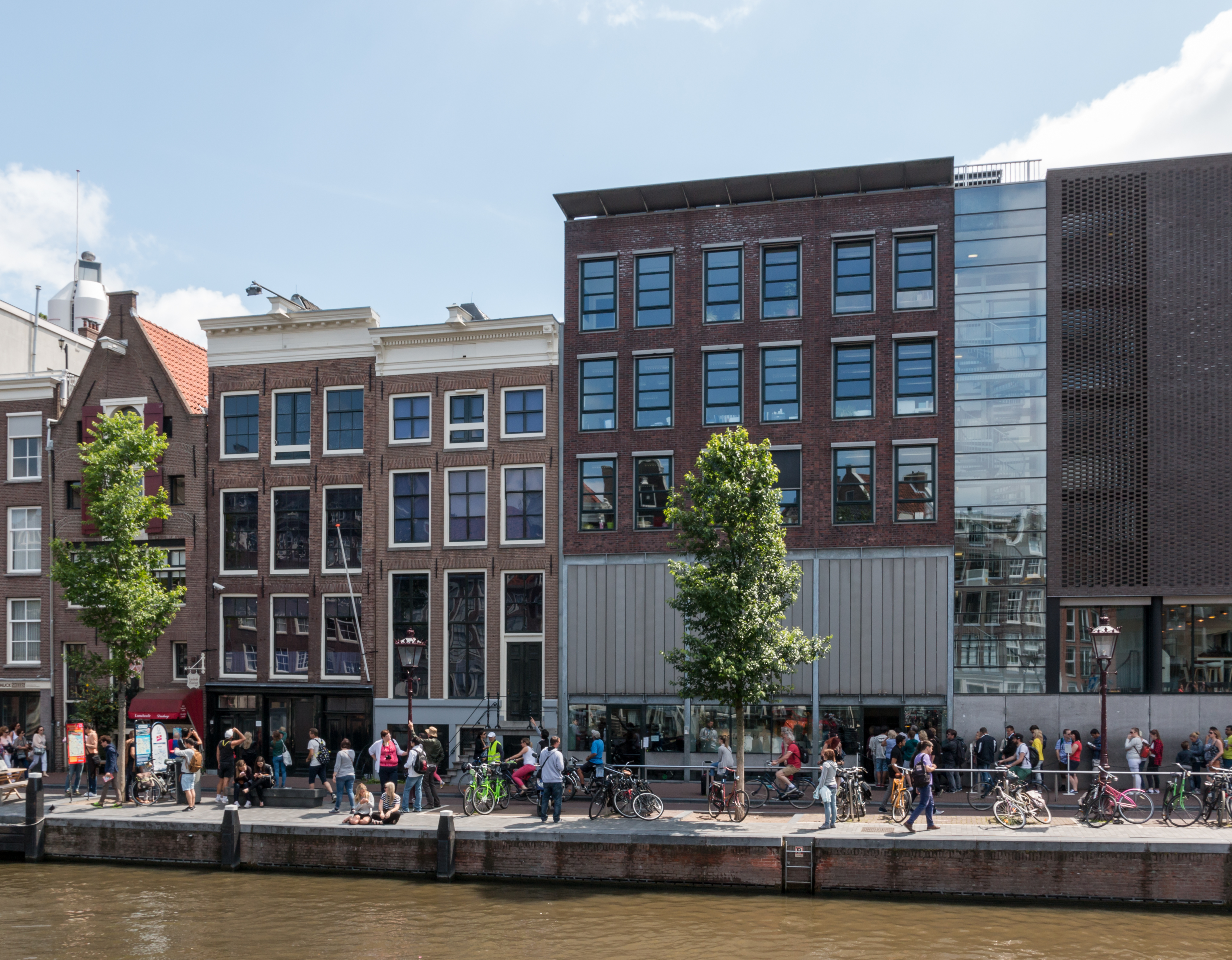 Uitzicht op historische bakstenen gebouwen langs het kanaal met menigten die langs de waterkant lopen, fietsen geparkeerd bij de reling