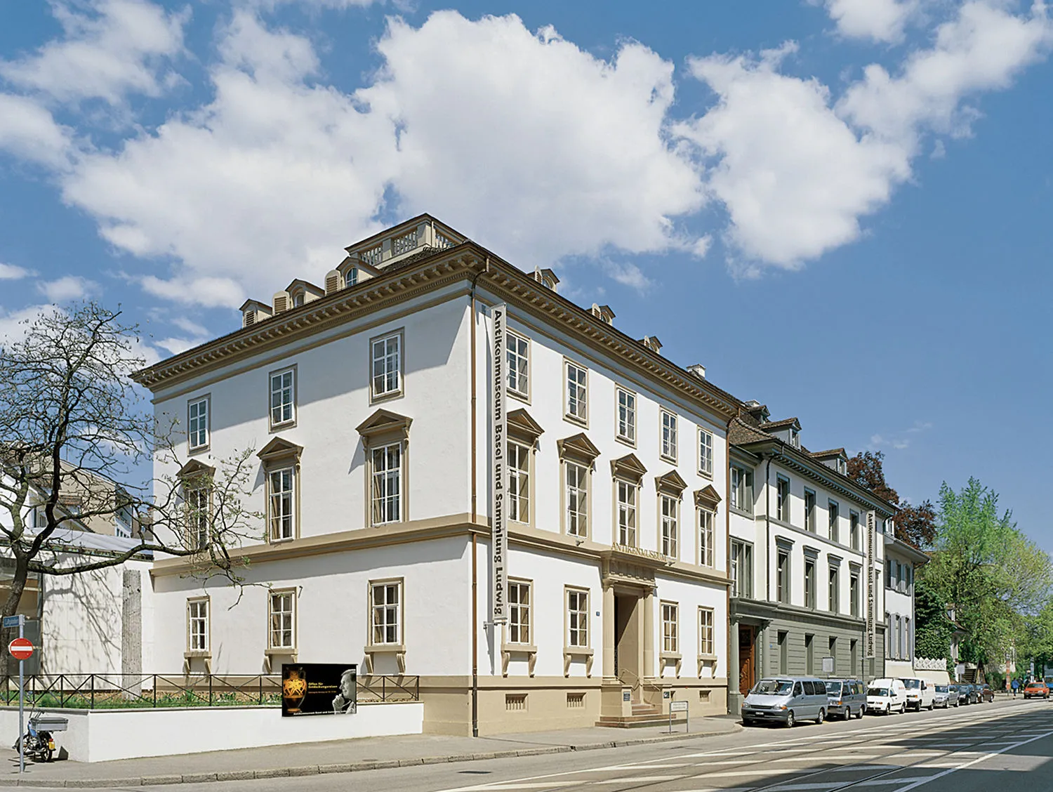 Biała klasyczna fasada budynku z wieloma oknami na tle błękitnego nieba z chmurami, Antikenmuseum Basel