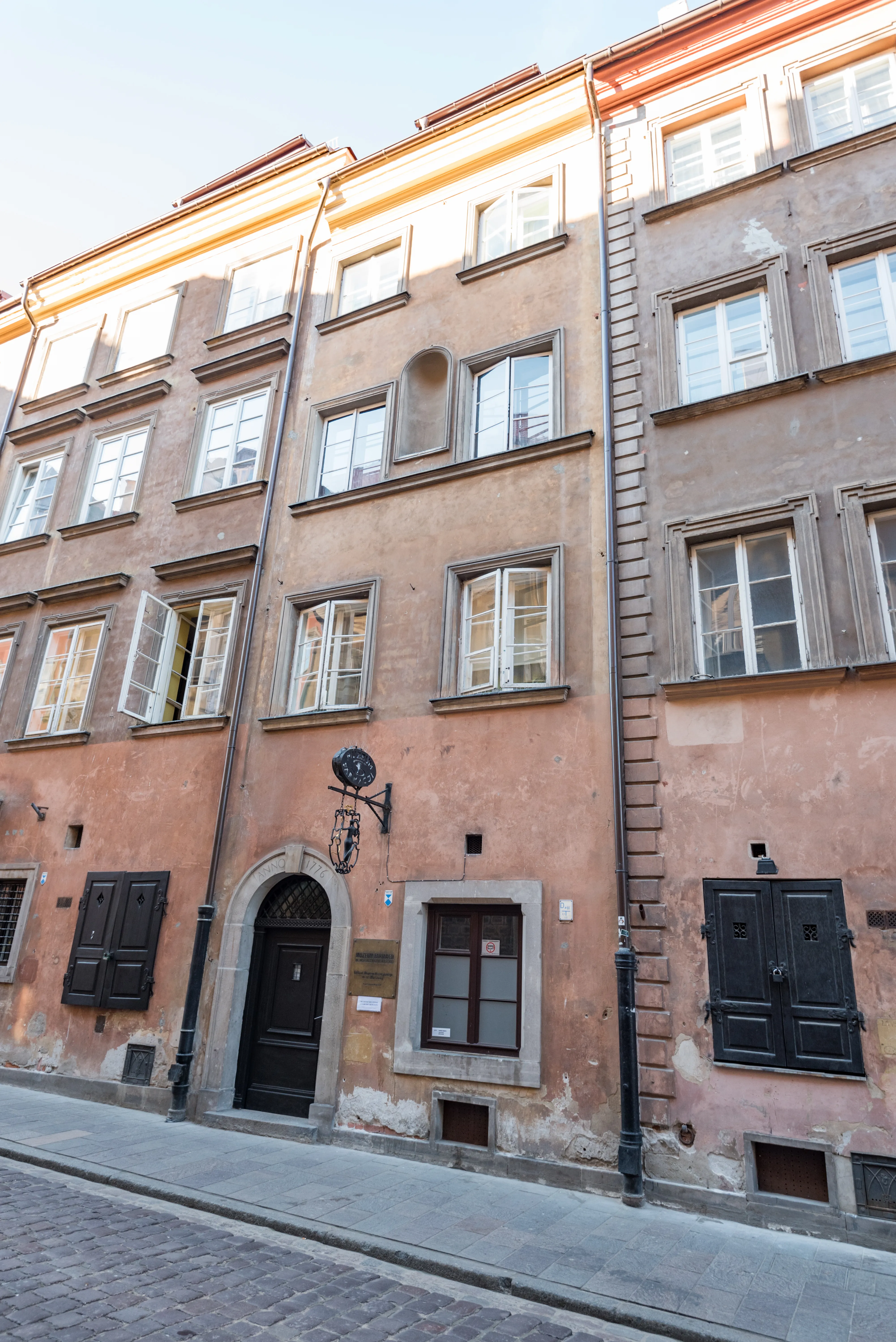 een historisch gebouw met een terracotta gevel, een boogvormige ingang en zwarte luiken aan een geplaveide straat