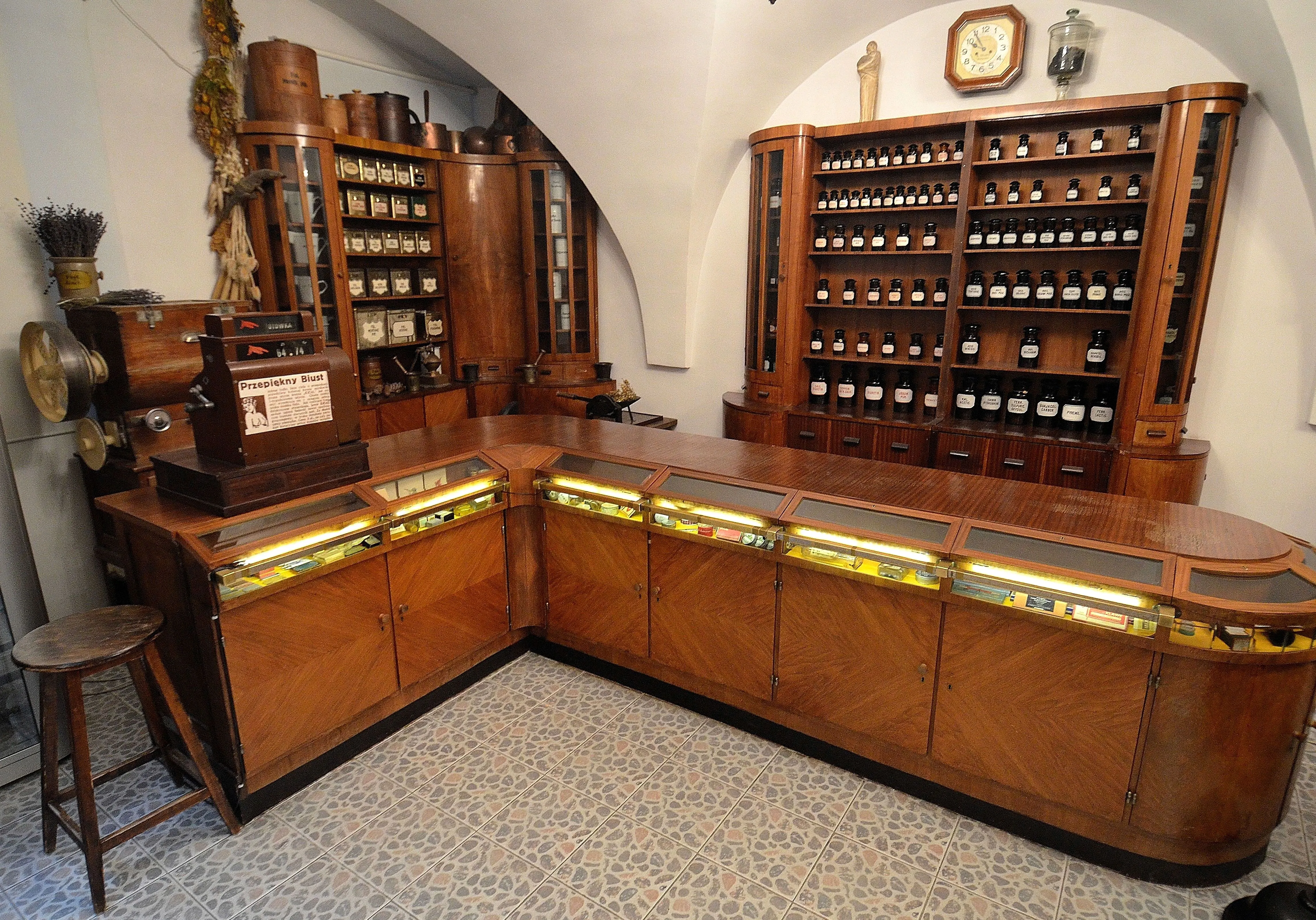 houten apotheekbalie met glazen vitrines en schappen vol flessen in een museum