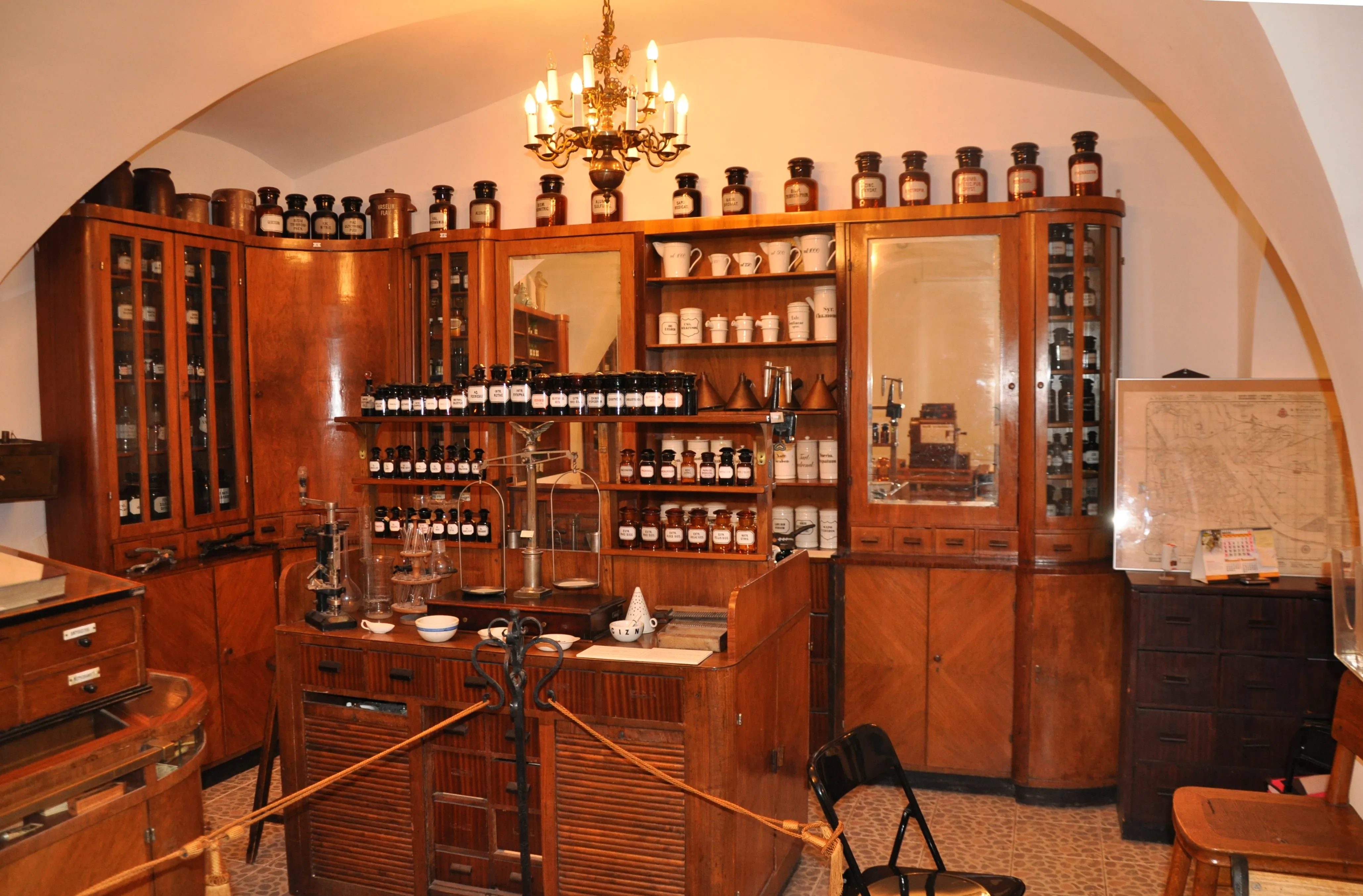 wooden pharmacy cabinets filled with bottles and jars, a central counter with laboratory equipment, and a chandelier