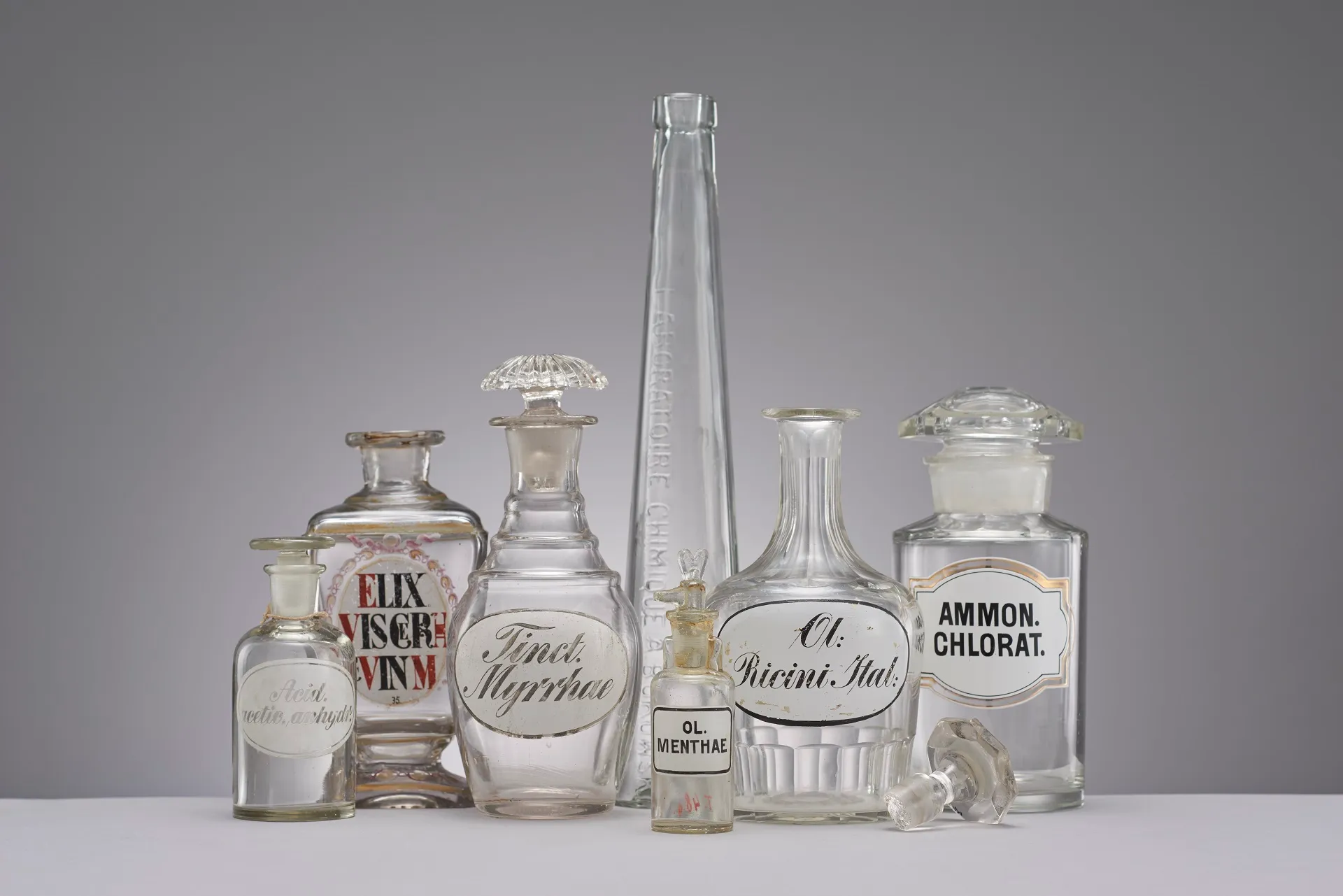 verzameling vintage apothekersglazen flessen en een hoge maatcilinder met etiketten