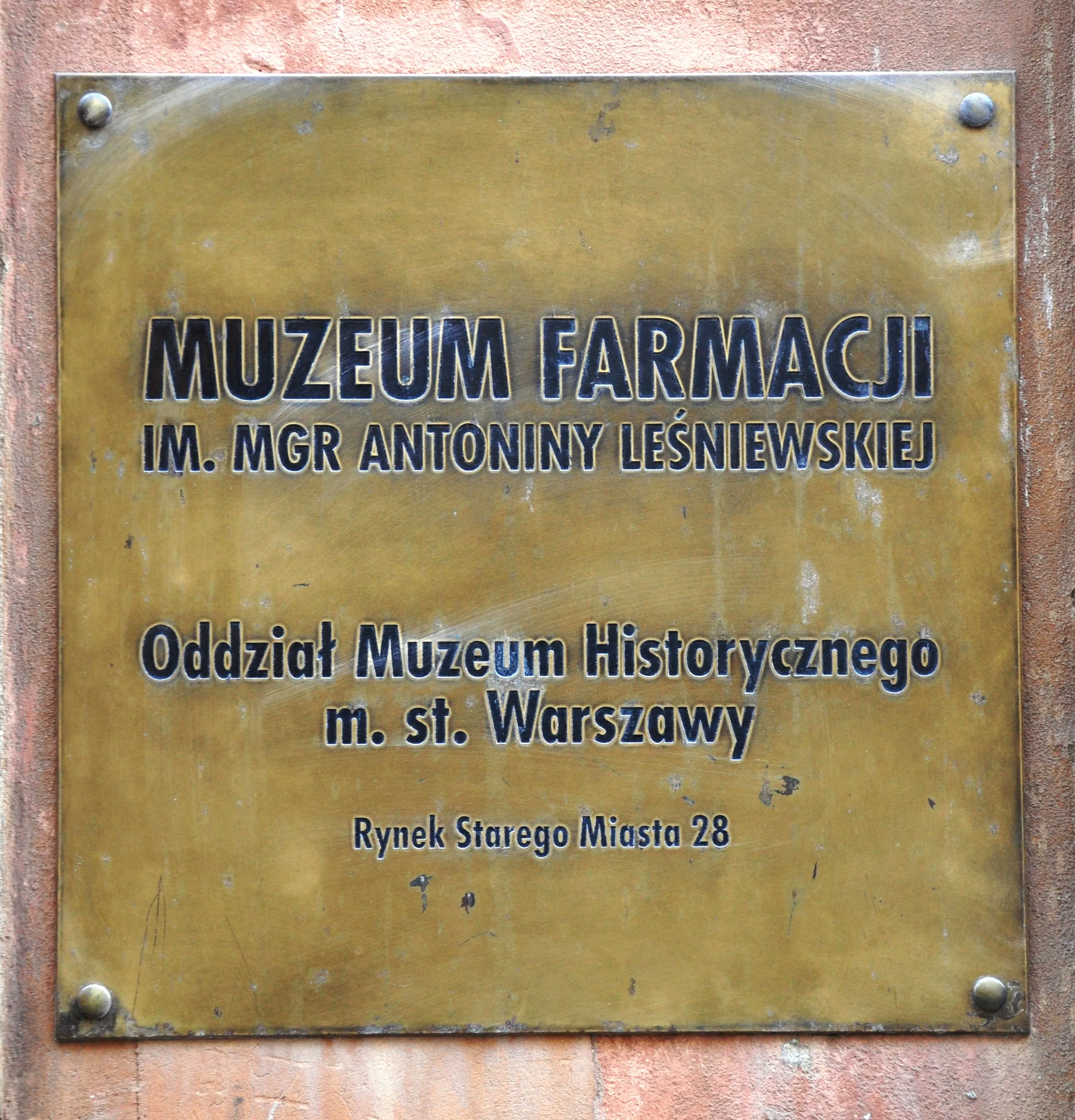 Bronzen plaquette met zwarte belettering met de tekst MUZEUM FARMACJI IM. MGR ANTONINY LEŚNIEWSKIEJ en informatie over de museumvestiging.