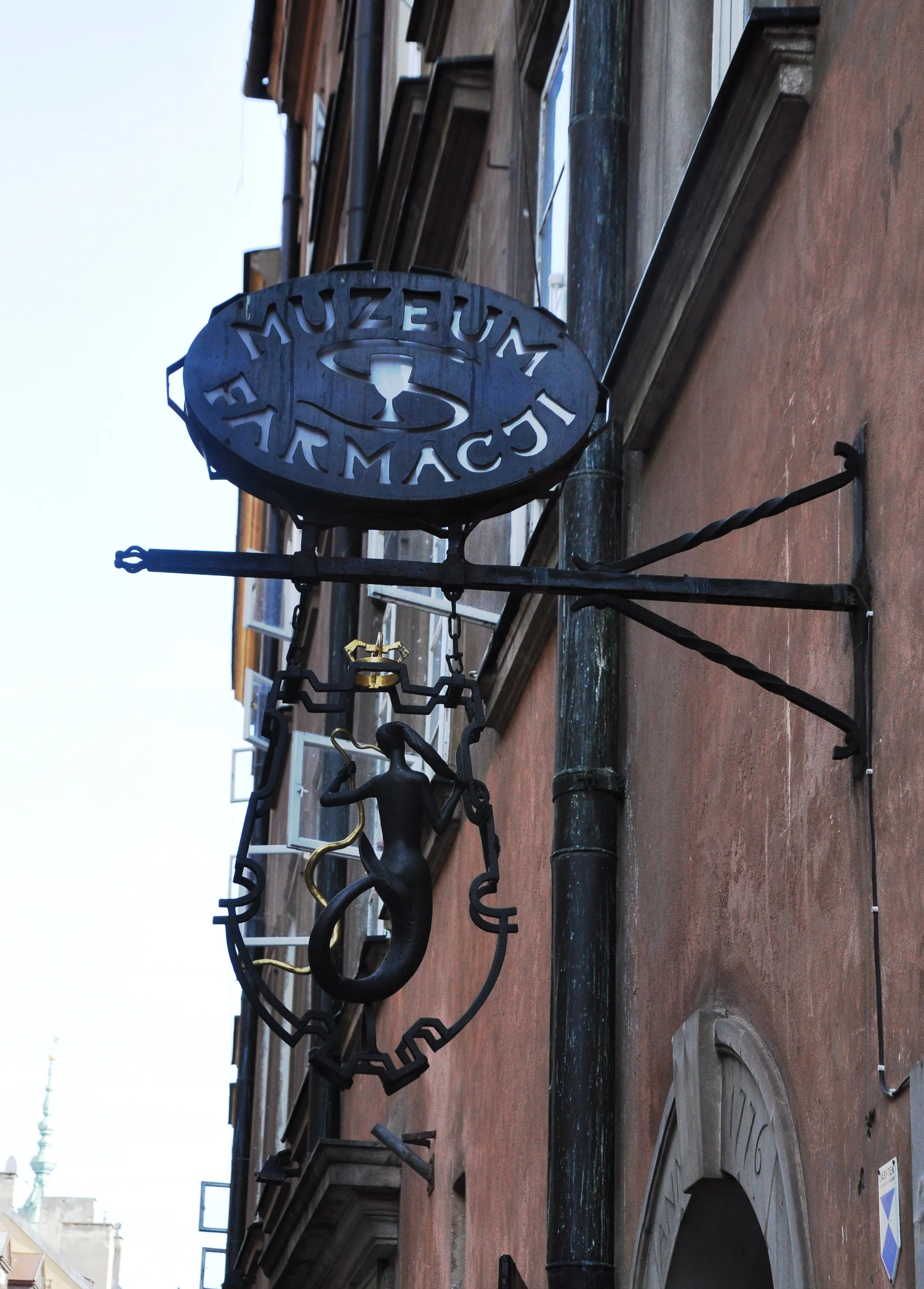 Black oval sign with 'MUZEUM FARMACJI' text and a figure, mounted on a building wall
