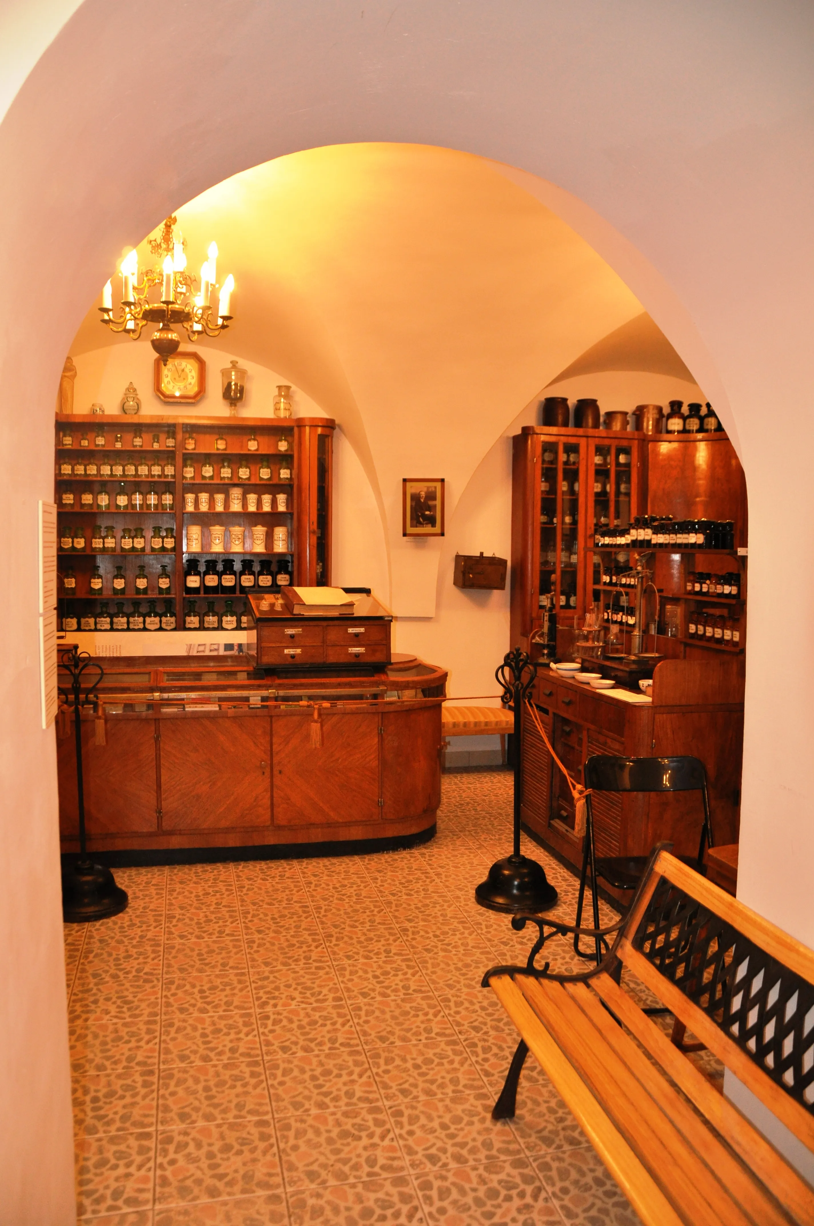 Interieur van een historische apotheek met houten balies, schappen vol flessen en een gewelfd plafond met een kroonluchter