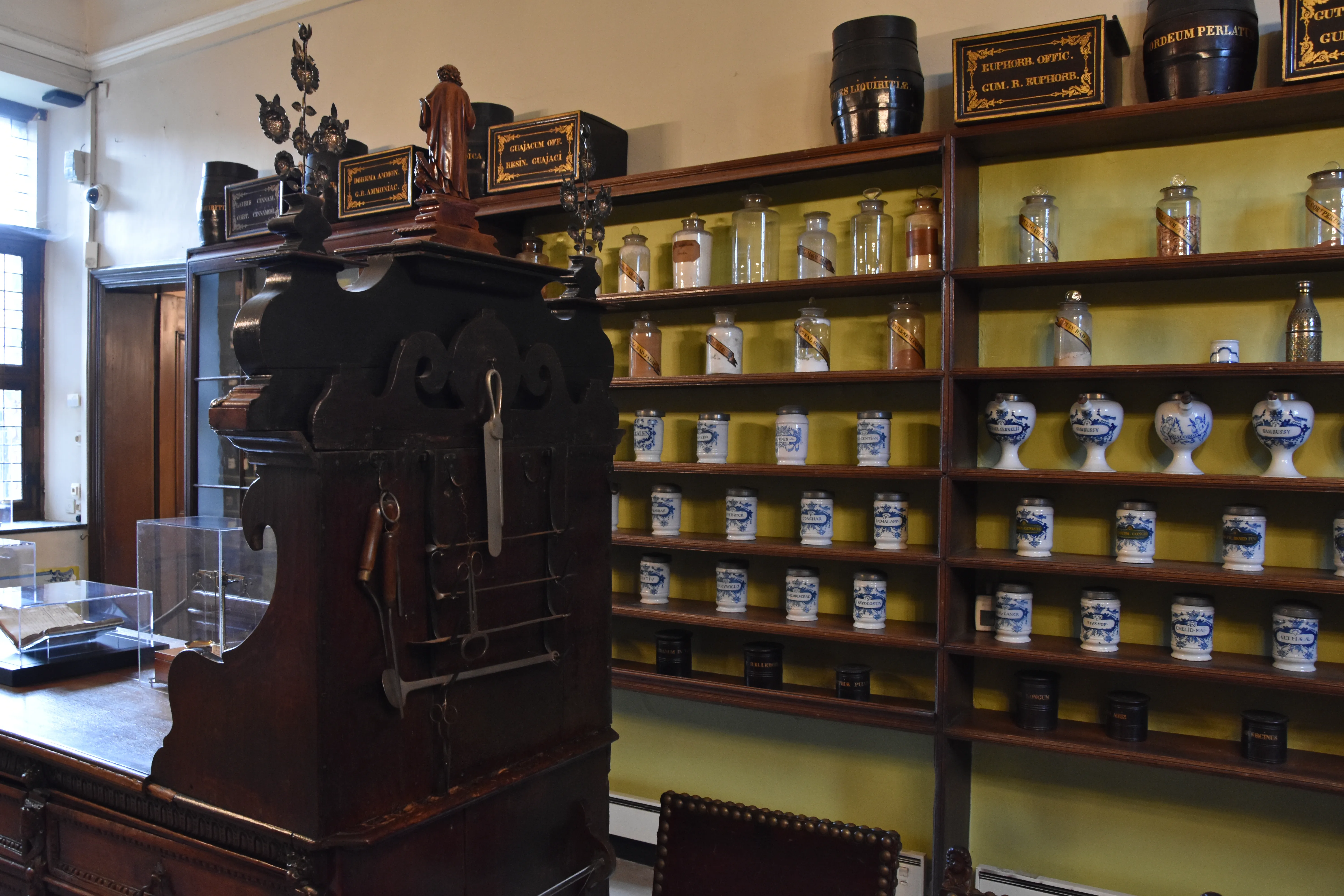 Interior de una farmacia histórica con estanterías de madera llenas de frascos de cerámica y vidrio, y un gran armario de madera oscura