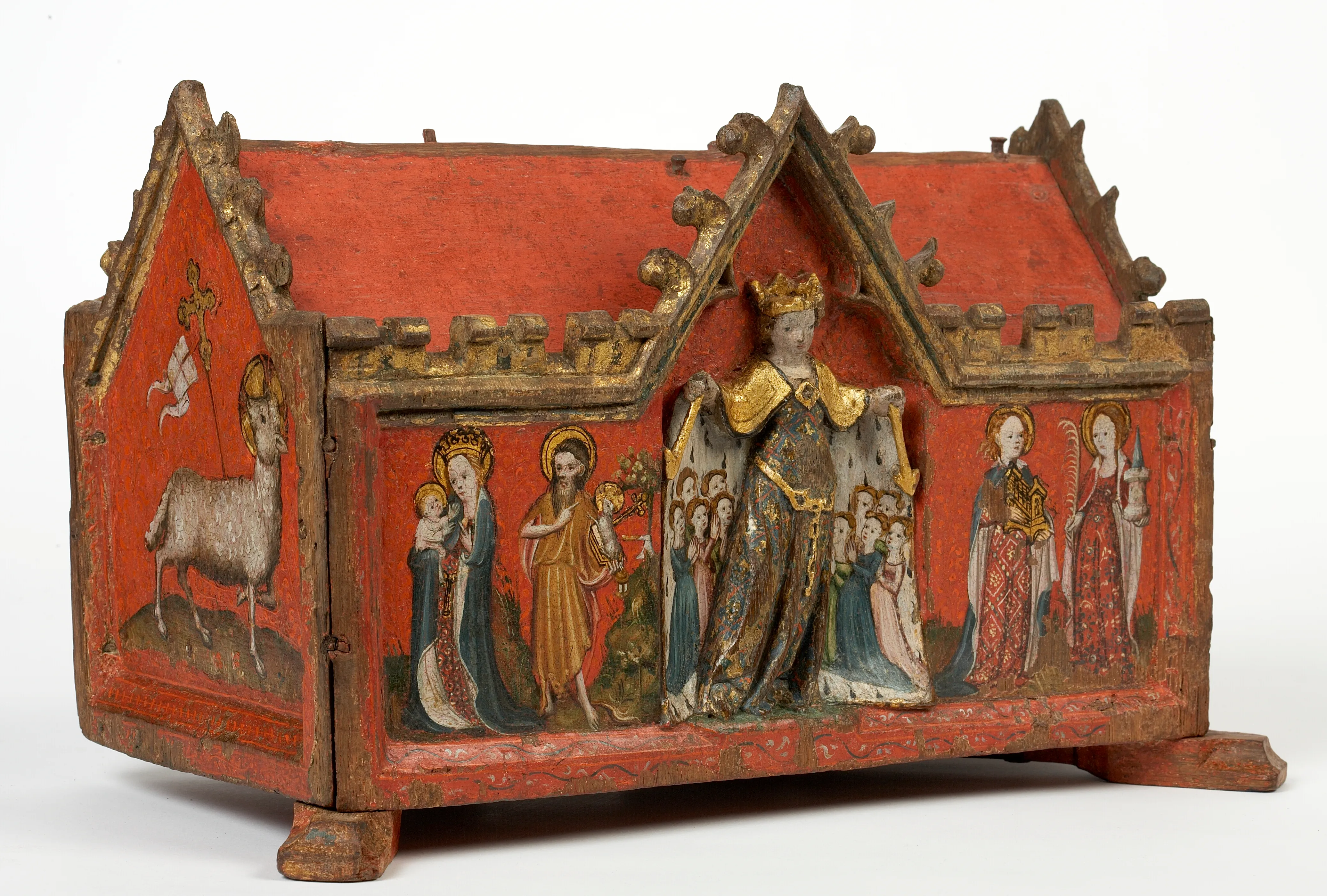 Retablo medieval de madera pintada con tejado a dos aguas rojo que representa a la Virgen María con el niño, una figura coronada, santos y un cordero.