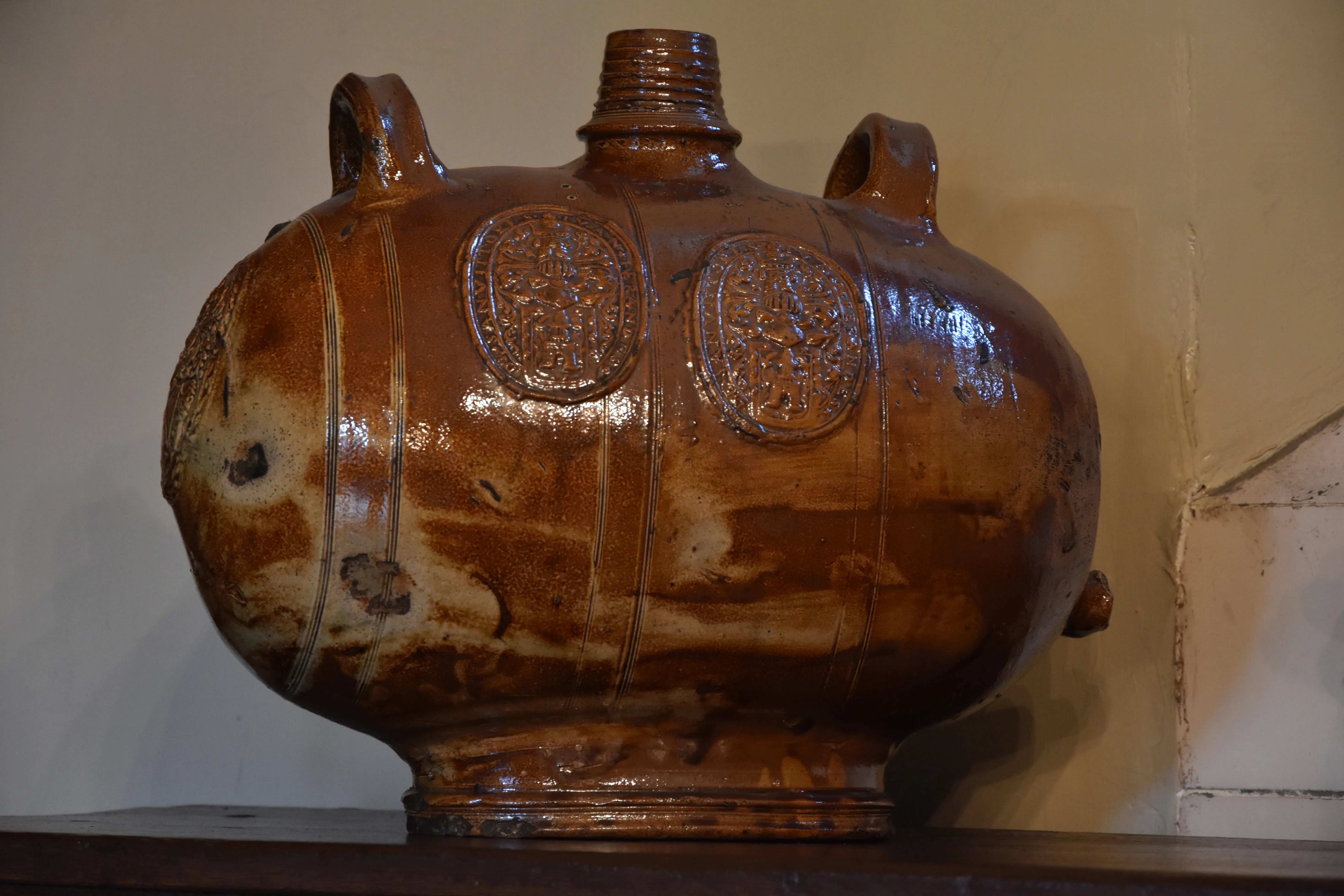 A large brown glazed ceramic apothecary jar with two loop handles and embossed decorative medallions on display