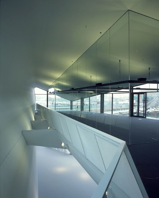 Modern interior space with glass walls, angular staircase, and large windows overlooking a city