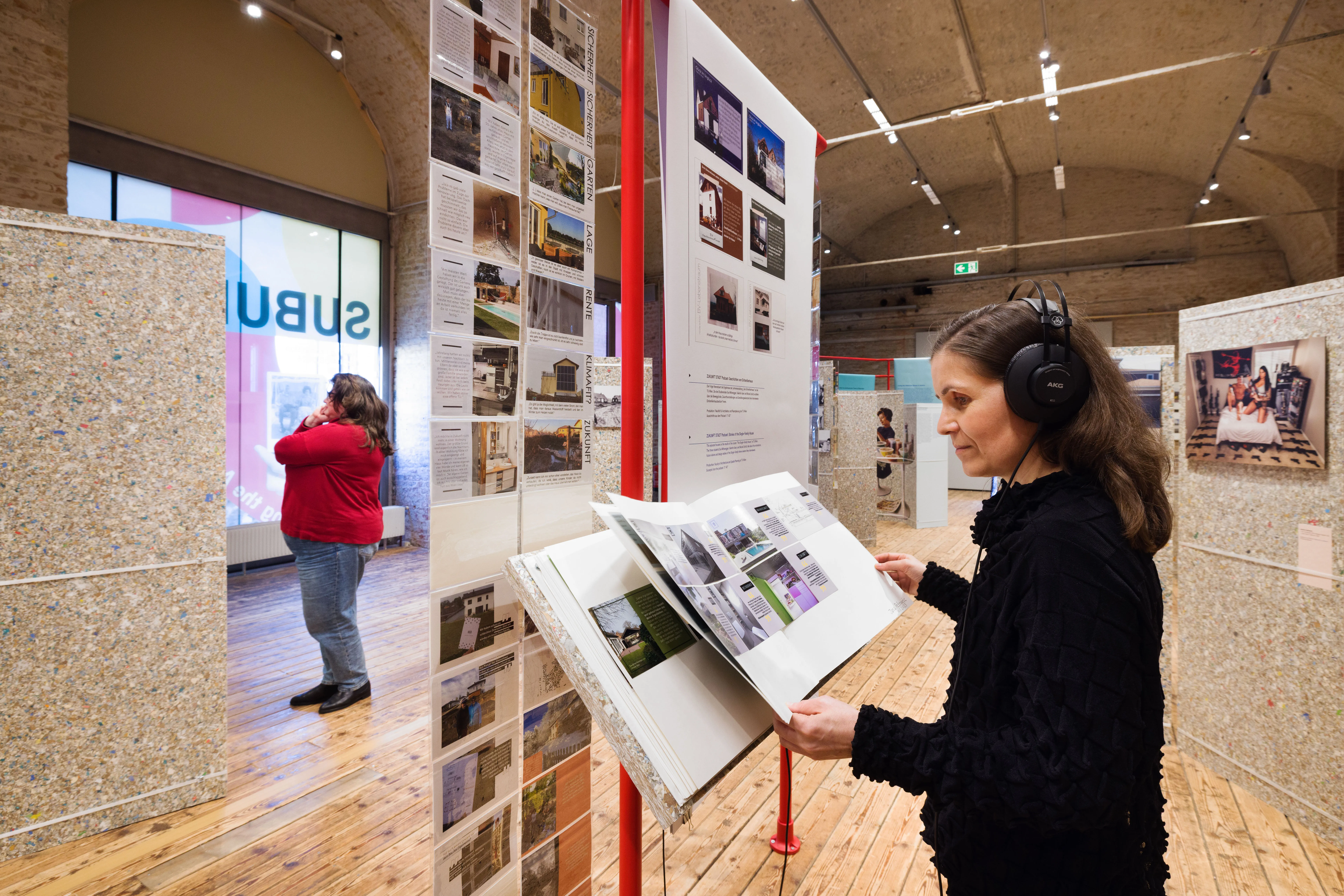 Bezoeker met koptelefoon kijkt naar een open display boek in een tentoonstellingsruimte met architecturale panelen en foto's aan de muren.