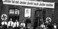 historical photograph of people standing in front of a building with swastika flags and a banner